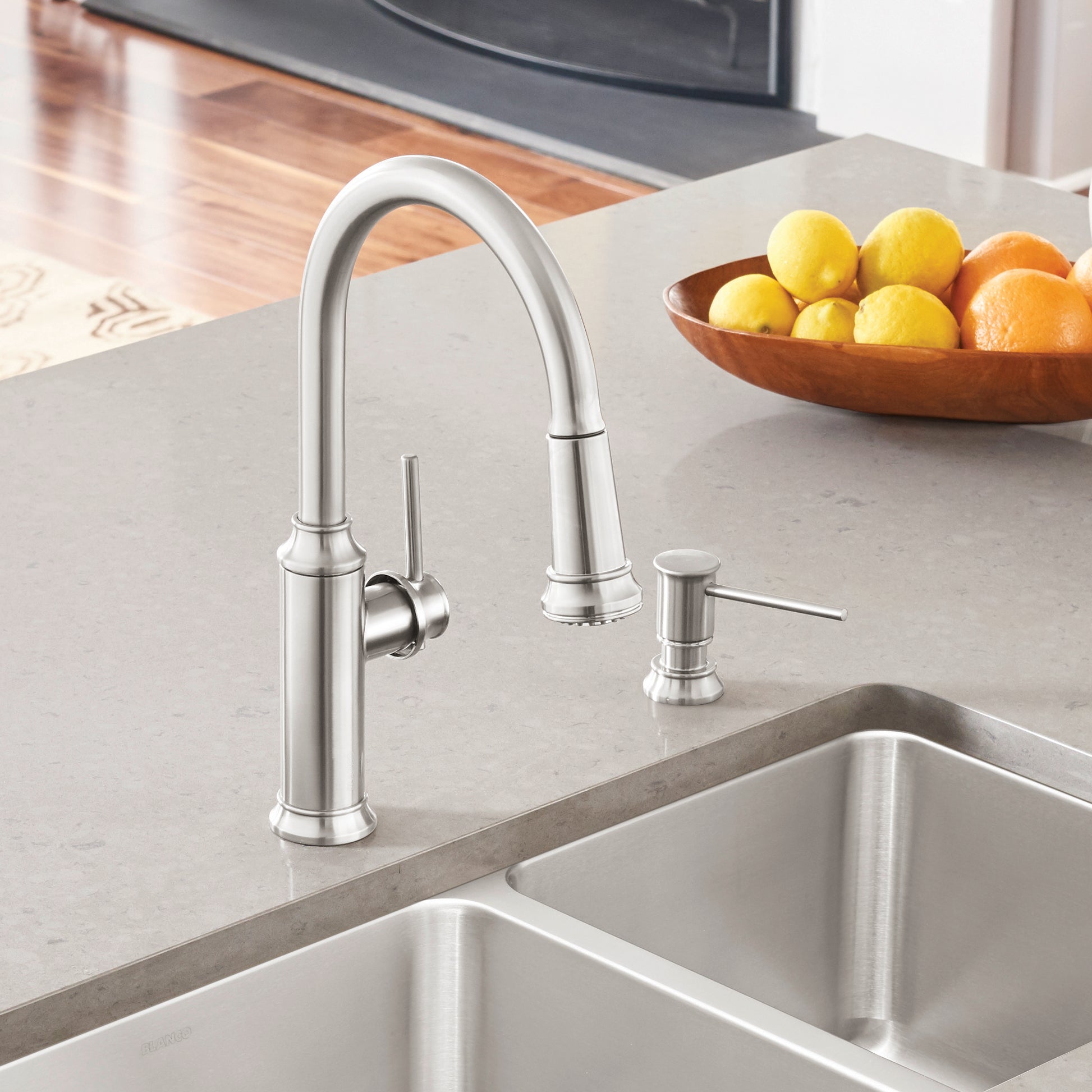 Stainless steel pull-down kitchen faucet with curved spout and lever handle above double sink basin.