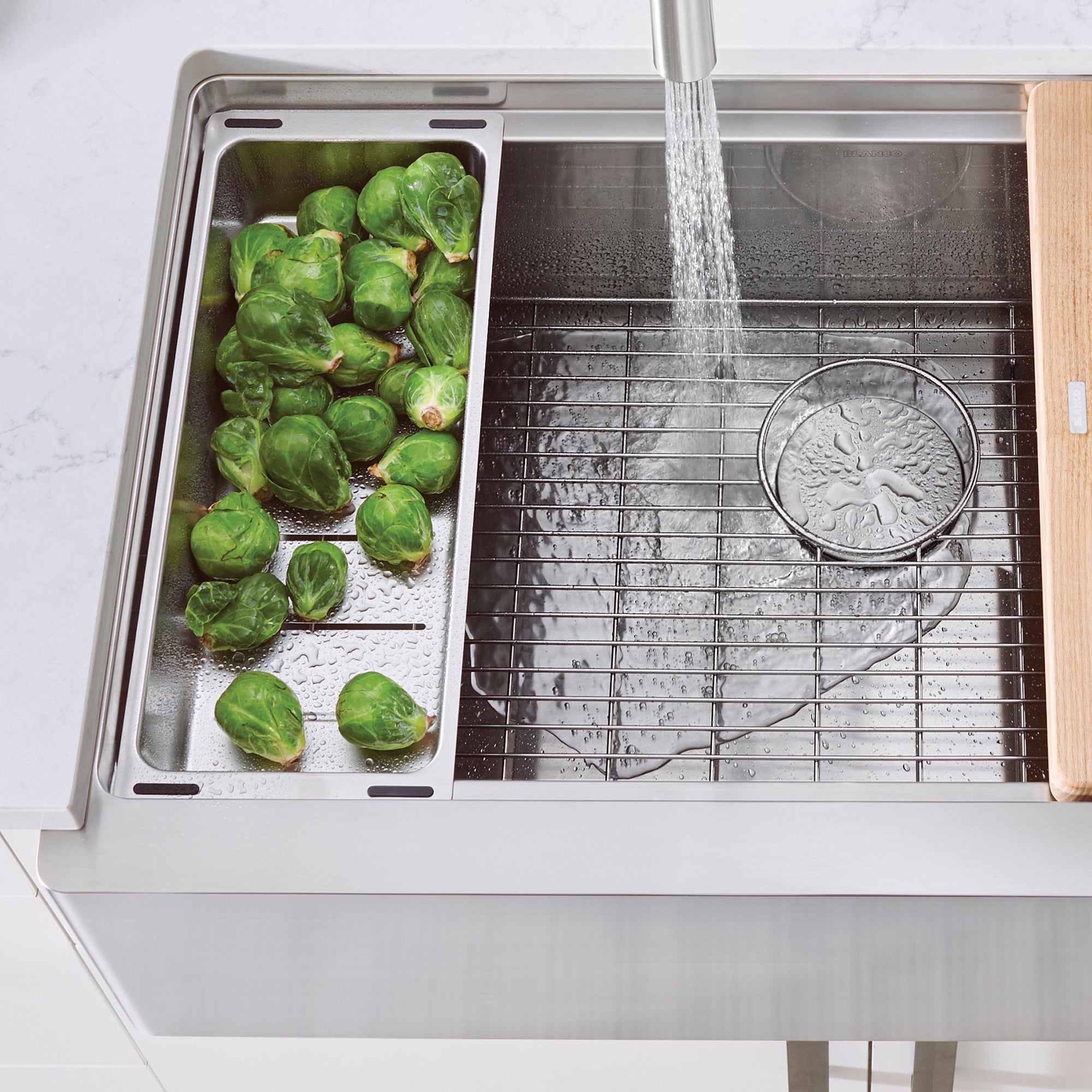 Stainless steel colander with perforated bowl positioned in sink basin with water draining over Brussels sprouts.