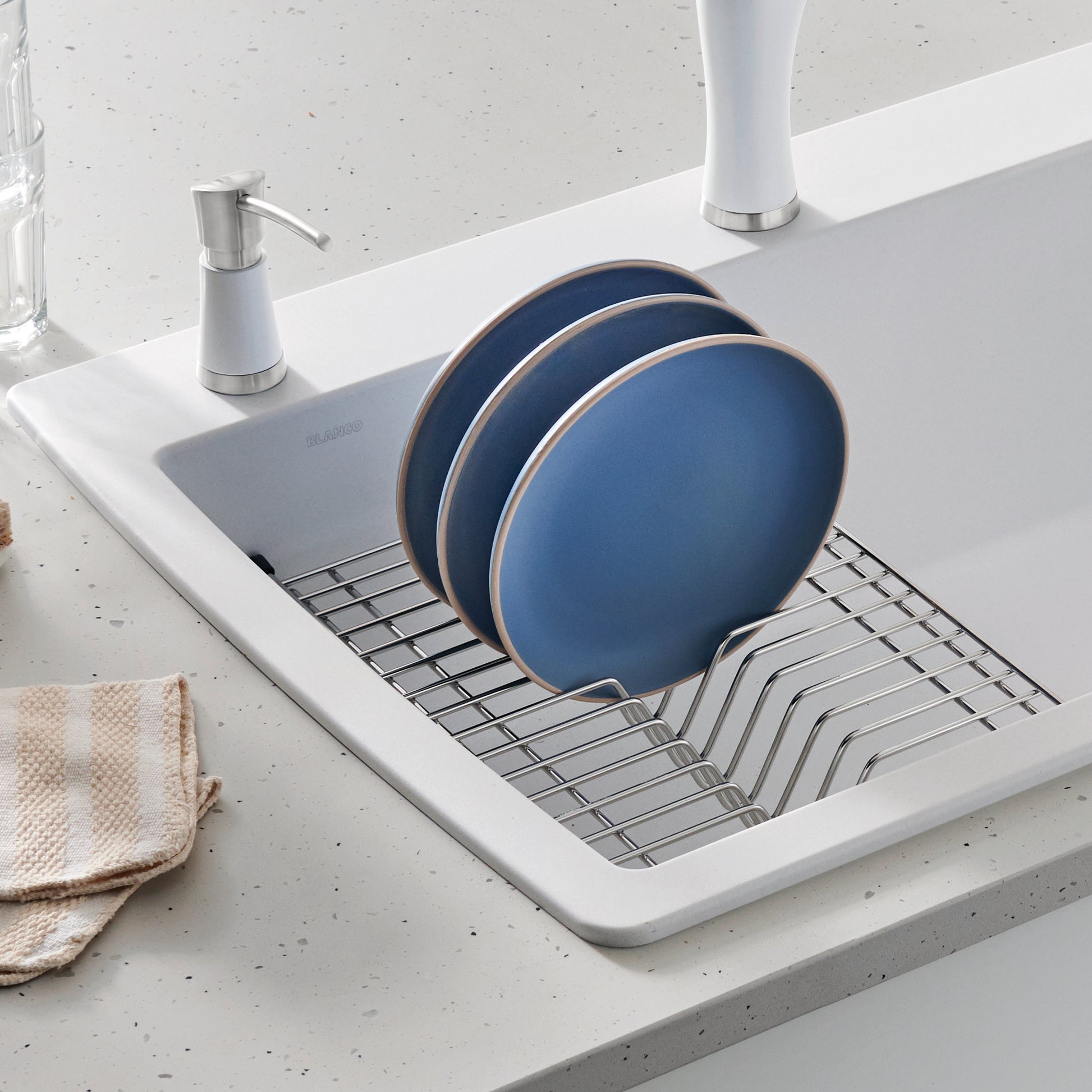 White floating dish rack with stainless steel grid holding three blue plates and utensil compartments, mounted in sink.