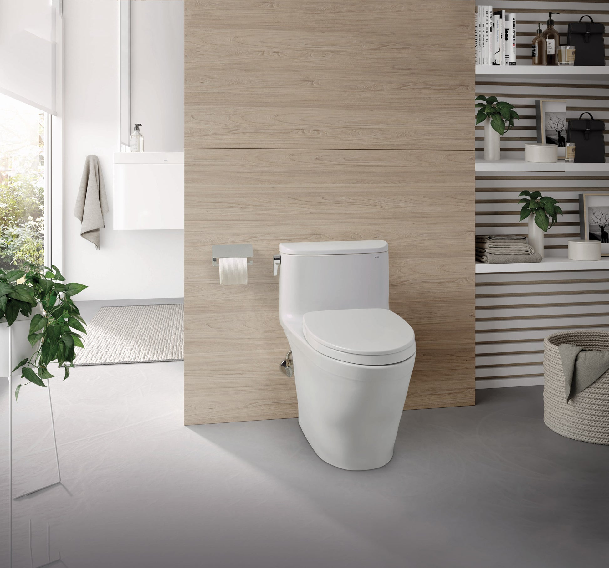 White elongated one-piece toilet with soft-close seat in a modern bathroom with wood-look wall and shelving.