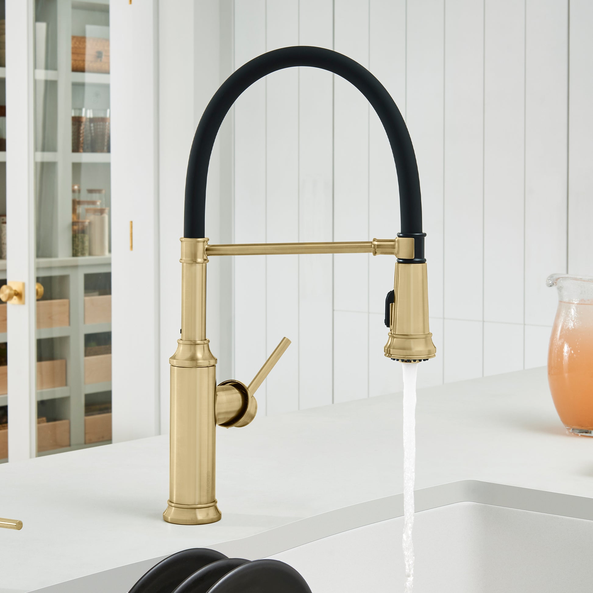 Satin gold kitchen faucet with black curved spout and handle, installed on white countertop.