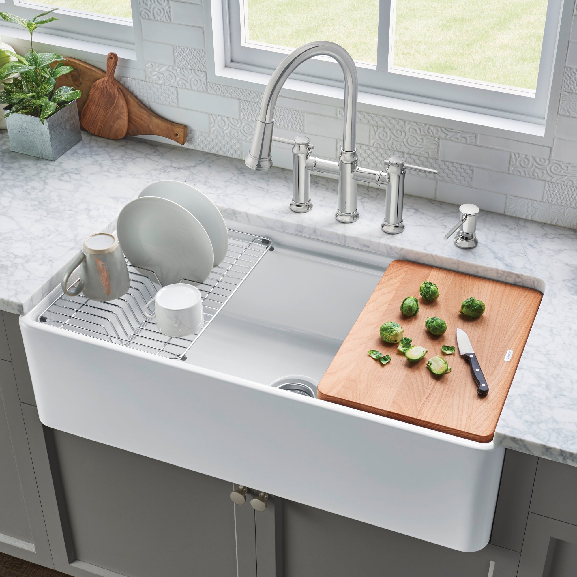 White ceramic apron front kitchen sink with single bowl, stainless steel faucet, and wooden cutting board.