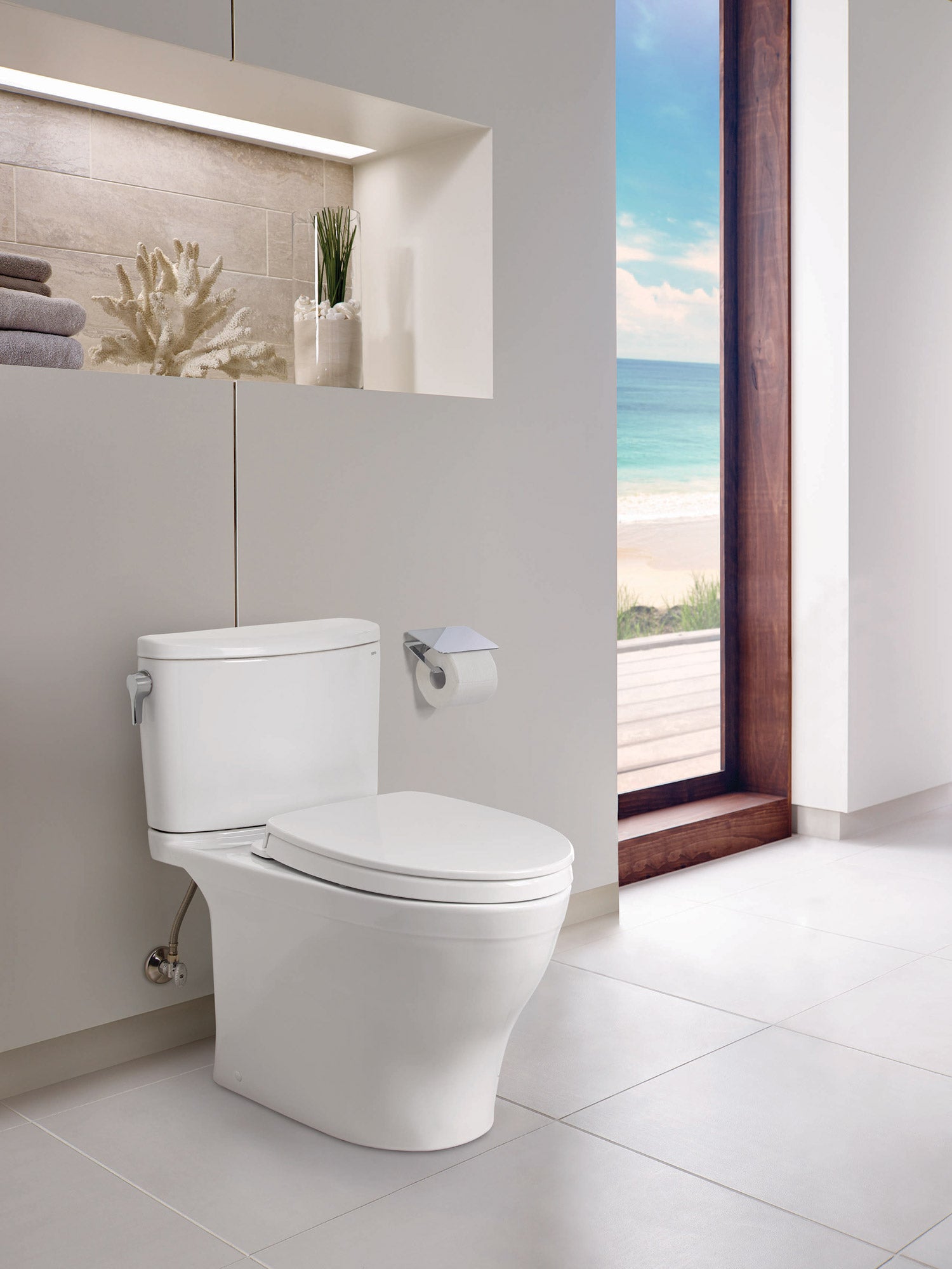 White two-piece elongated toilet with soft-close seat in a modern bathroom with ocean view.