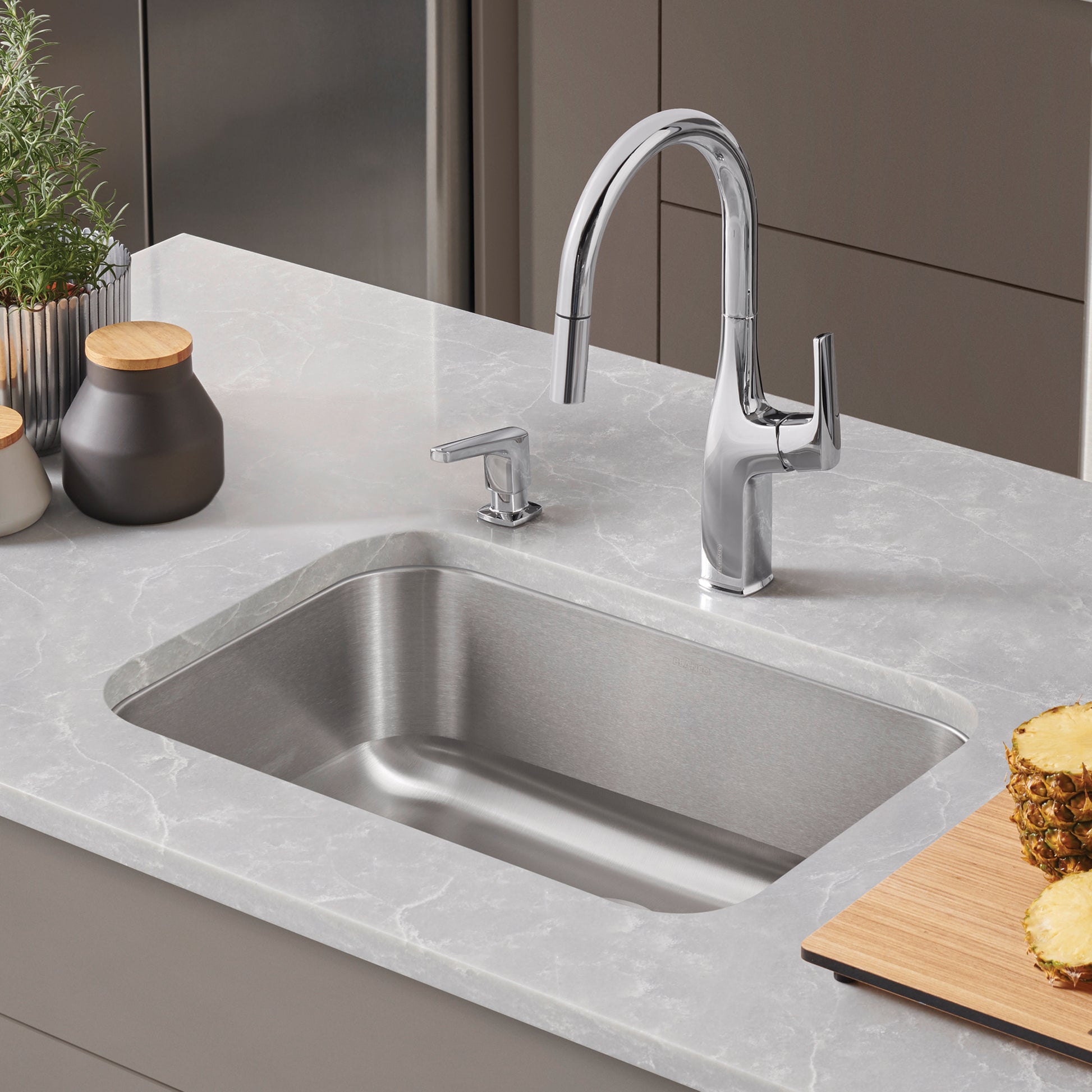Stainless steel rectangular undermount sink with chrome pull-down faucet and soap dispenser on light gray countertop.