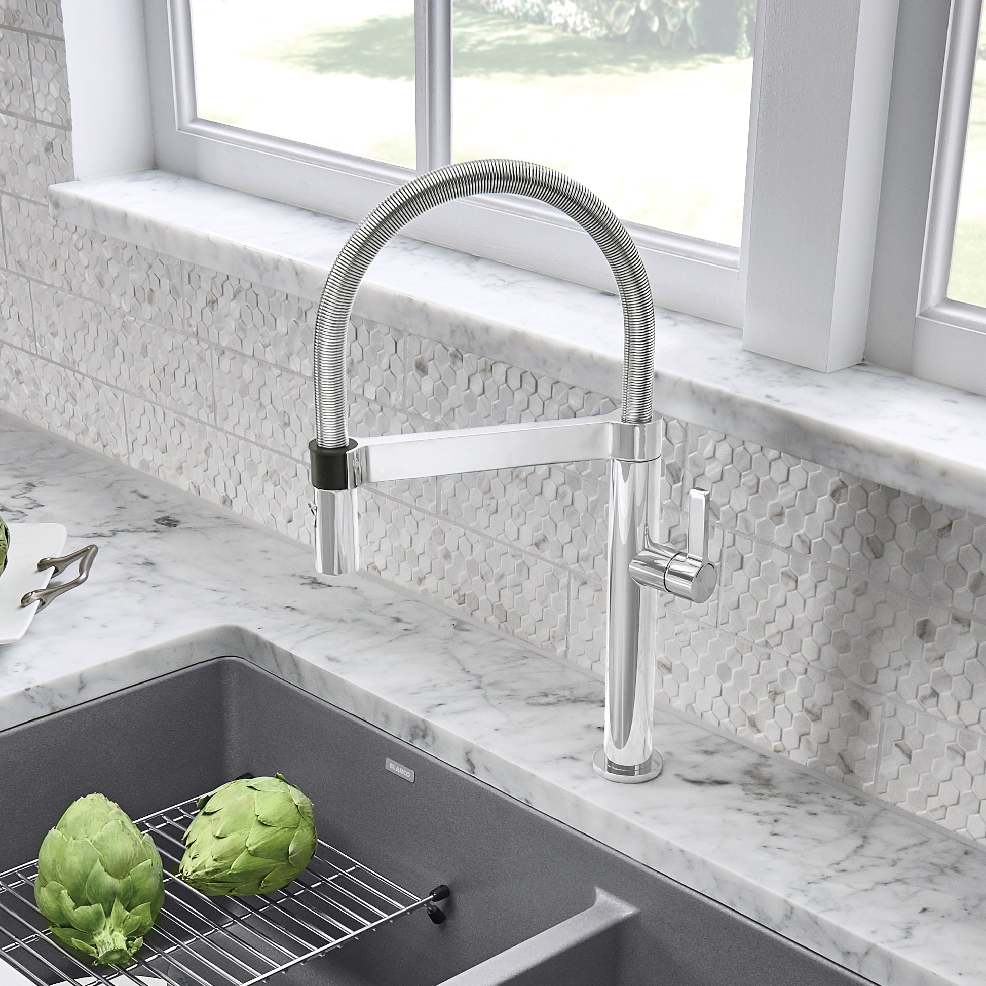 Chrome pull-down kitchen faucet with flexible hose and single lever handle mounted on marble countertop.