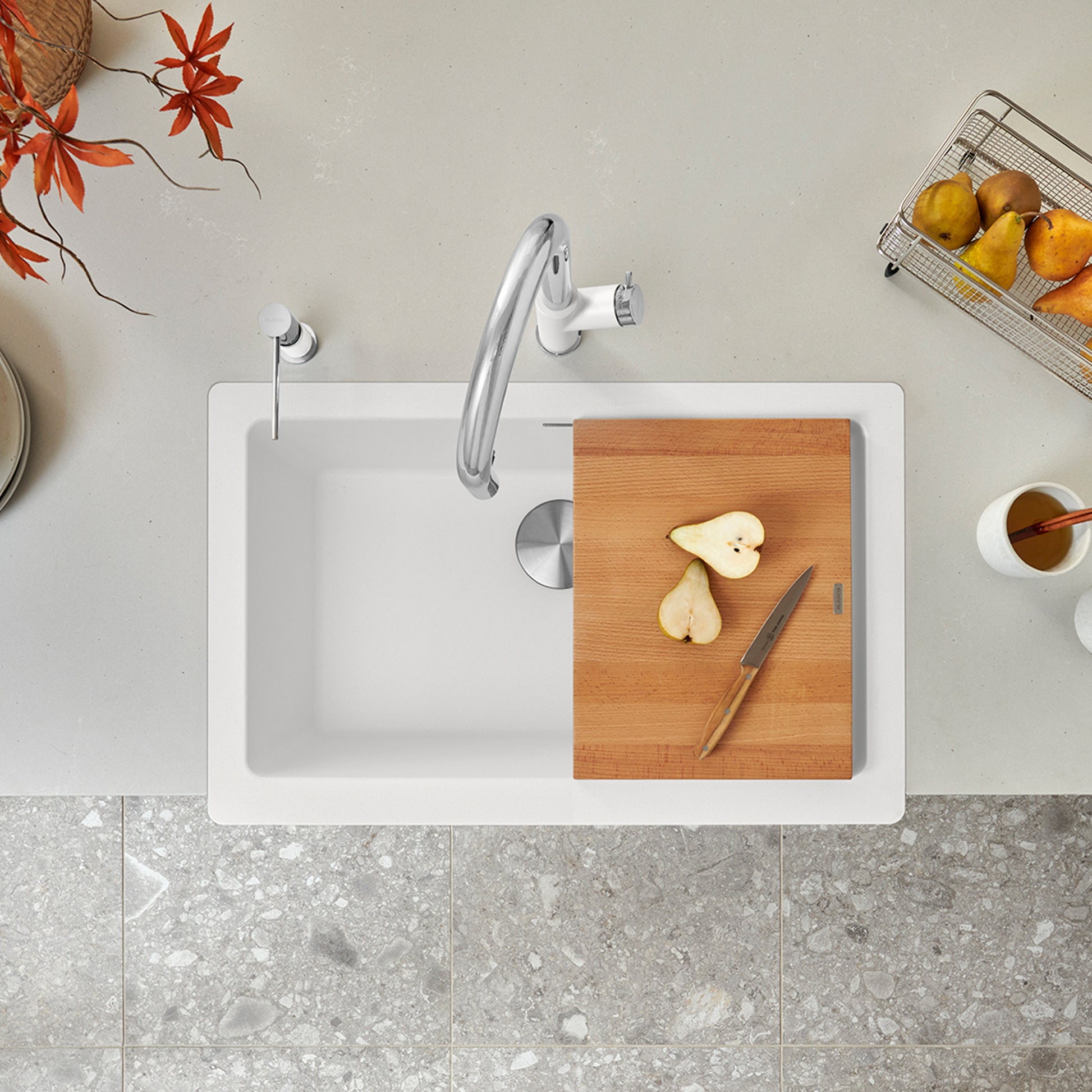 White farmhouse apron sink with single basin, chrome faucet, and wooden cutting board staged with produce and kitchen accesso