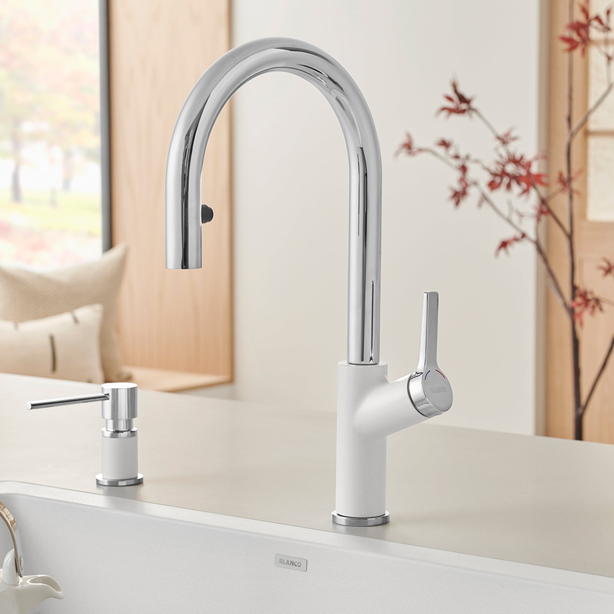 Chrome and white pull-down kitchen faucet with curved spout and single lever handle on white countertop.