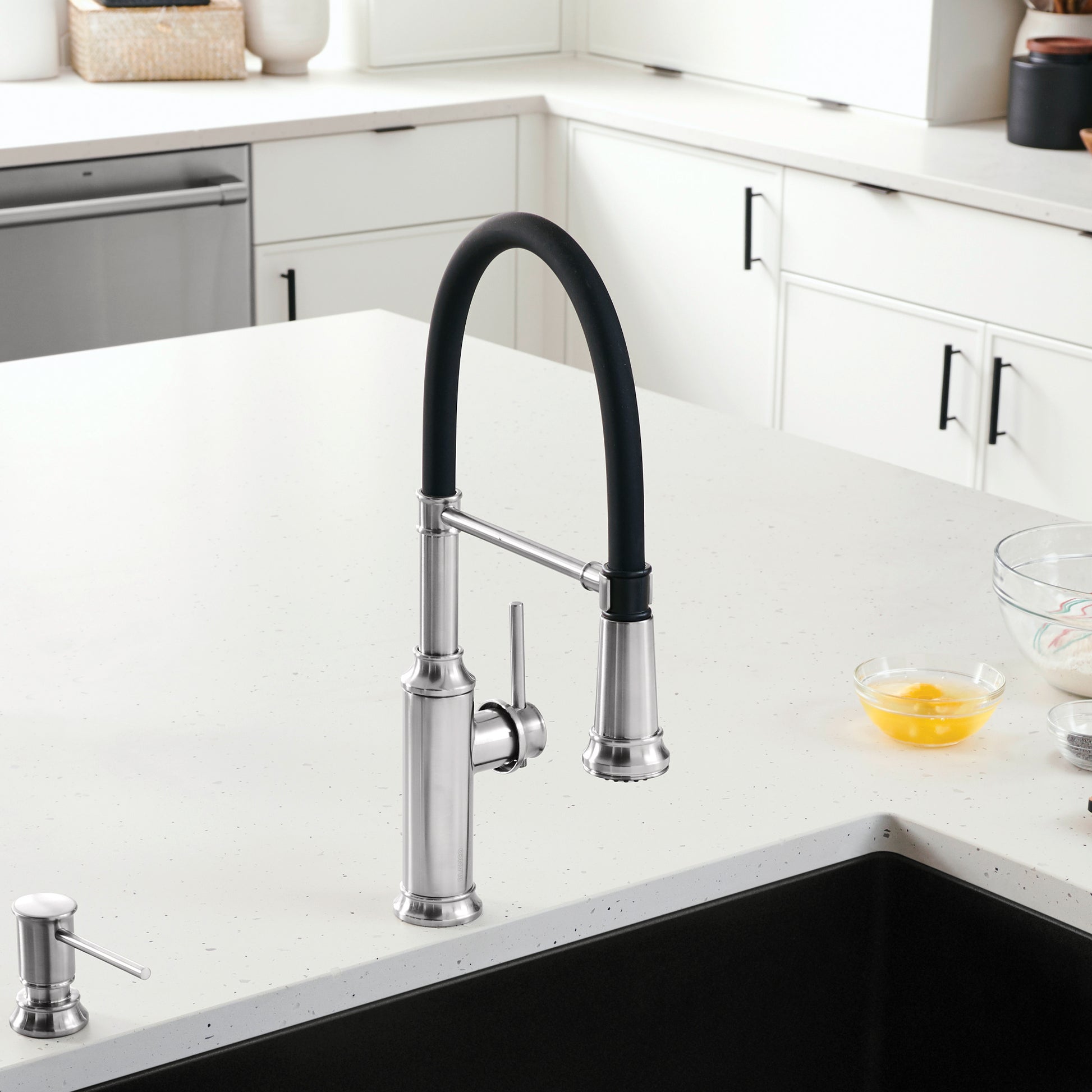 Stainless steel kitchen faucet with black flexible hose and pull-down sprayer mounted on white countertop.