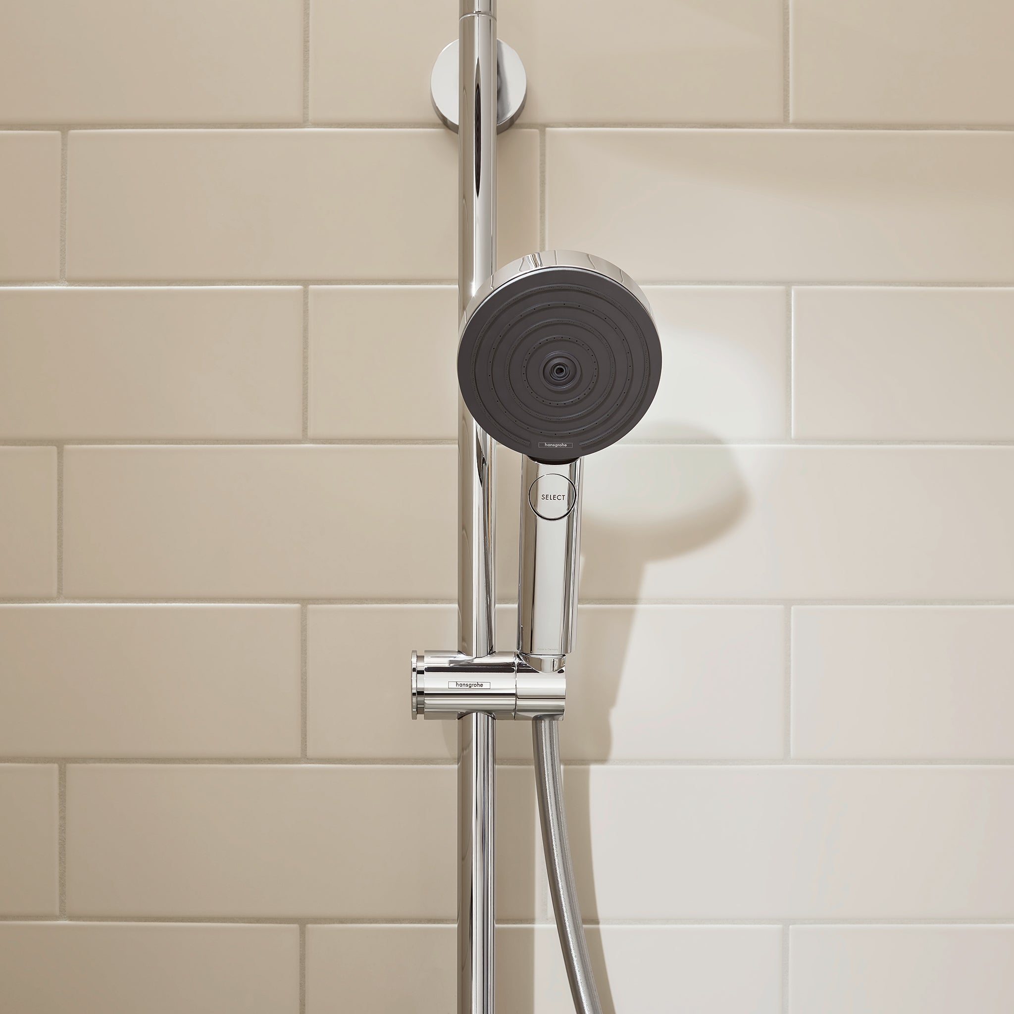 Chrome handshower with black circular showerhead and adjustment dial mounted on vertical rail against tiled wall.