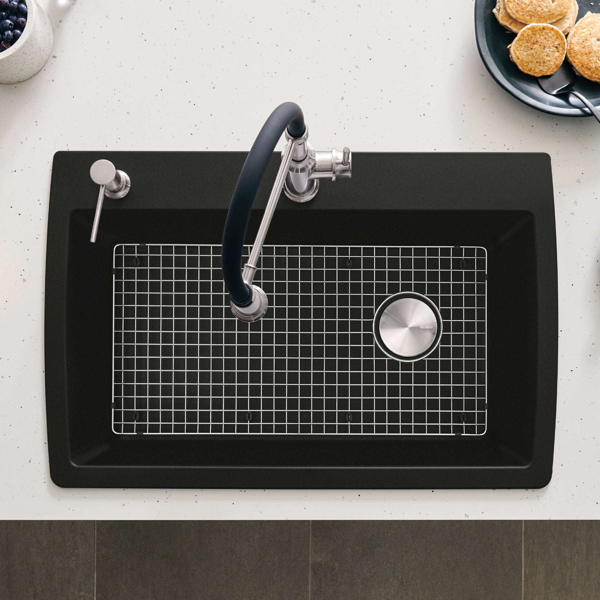 Stainless steel sink grid with fine mesh pattern positioned in black kitchen sink basin.