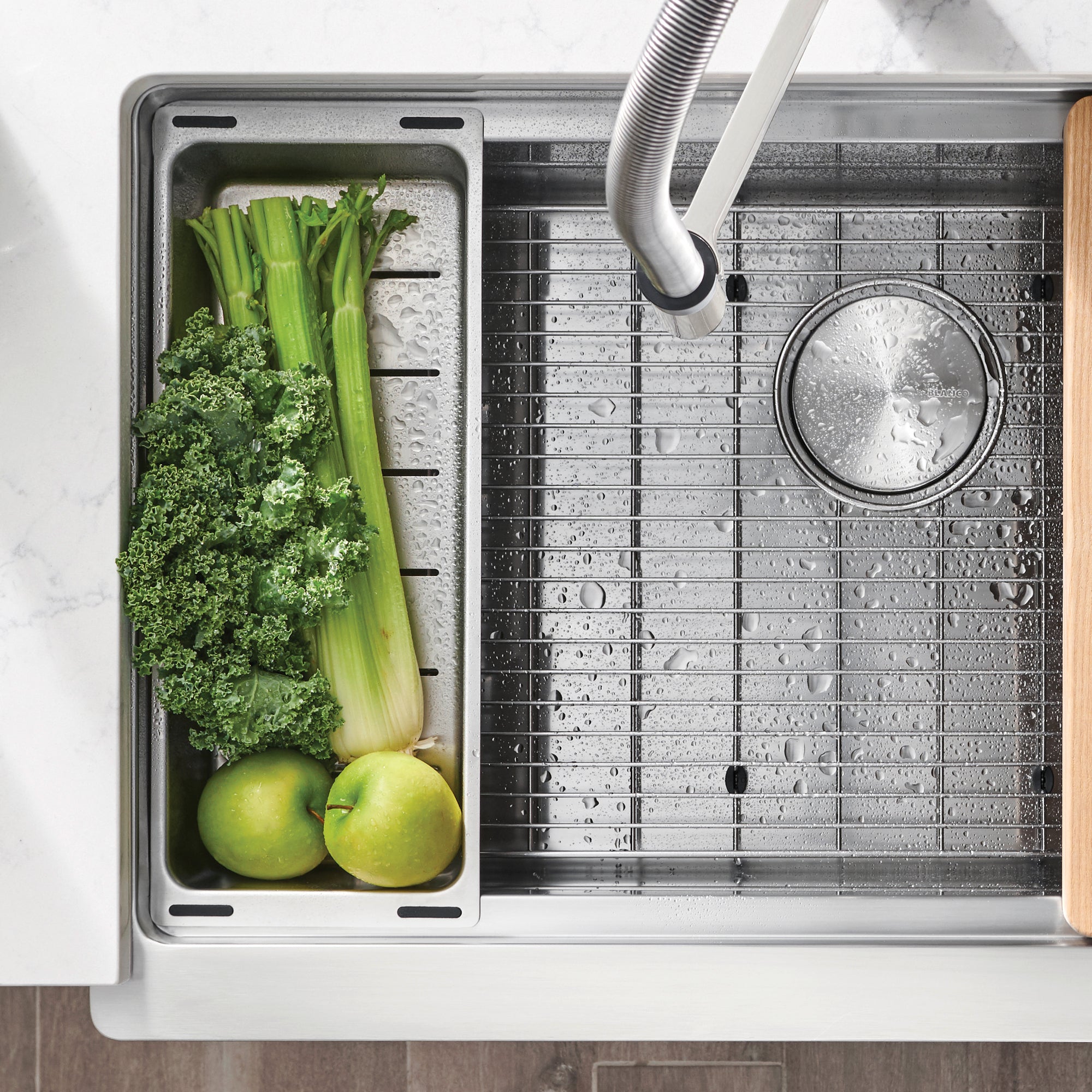 Stainless steel colander with perforated surface and rim, positioned in sink basin next to drainer section.