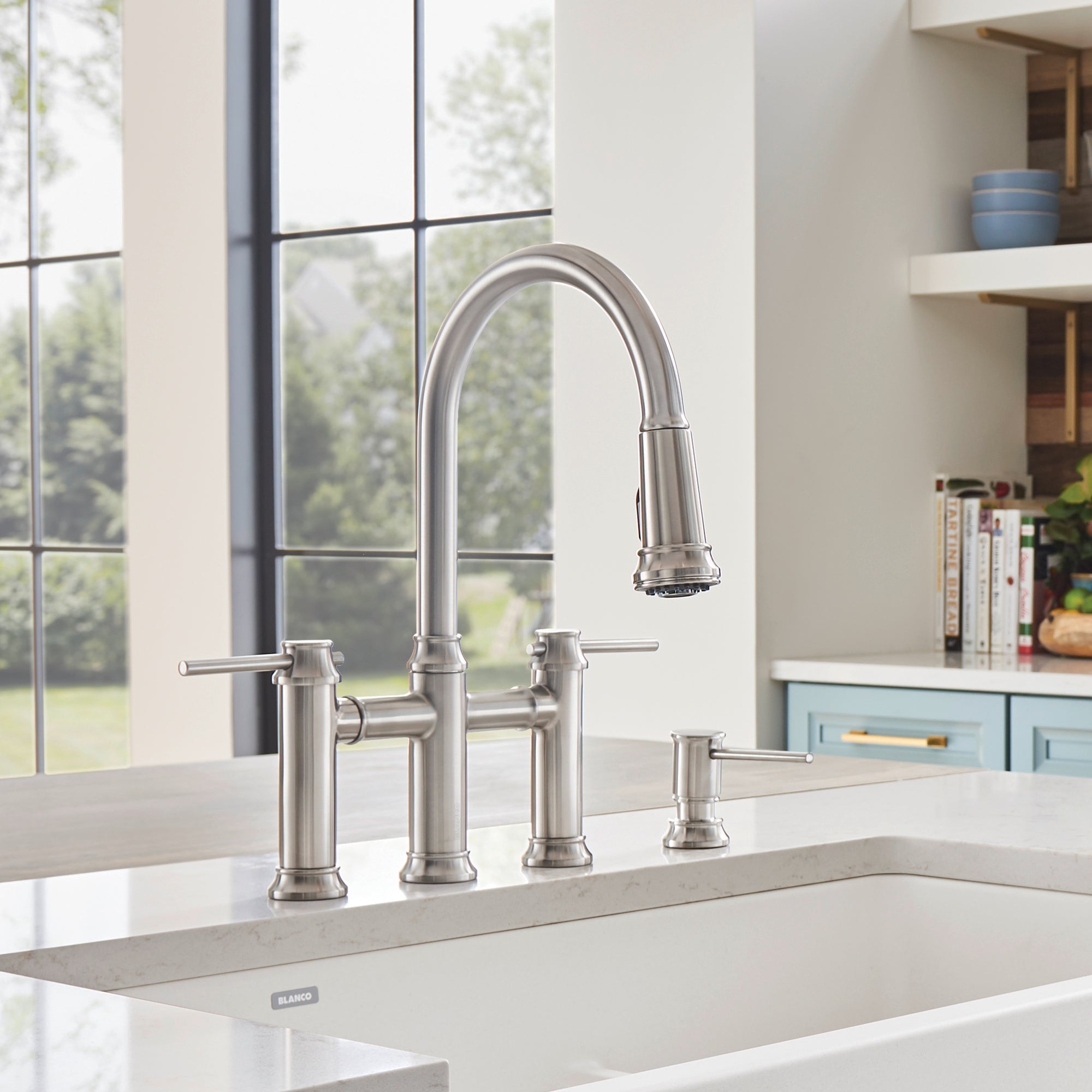 Stainless steel bridge pull-down kitchen faucet with curved spout and dual side handles mounted on white countertop.