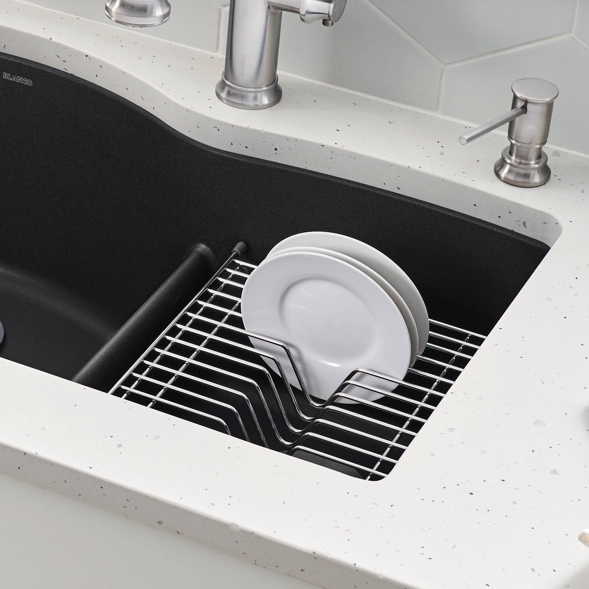 Stainless steel dish rack with white plates inside black kitchen sink basin.
