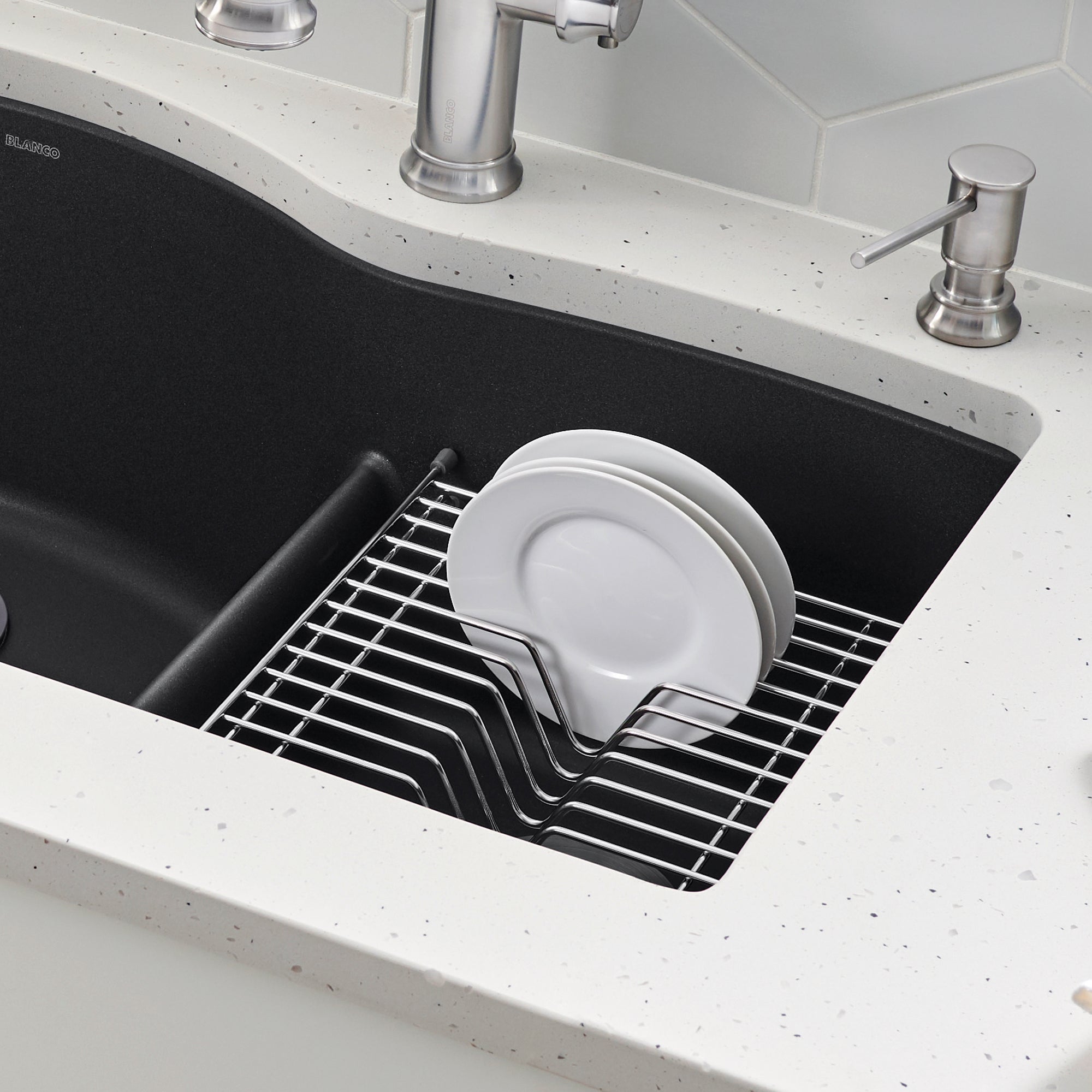Stainless steel dish rack with white plates inside black kitchen sink basin.