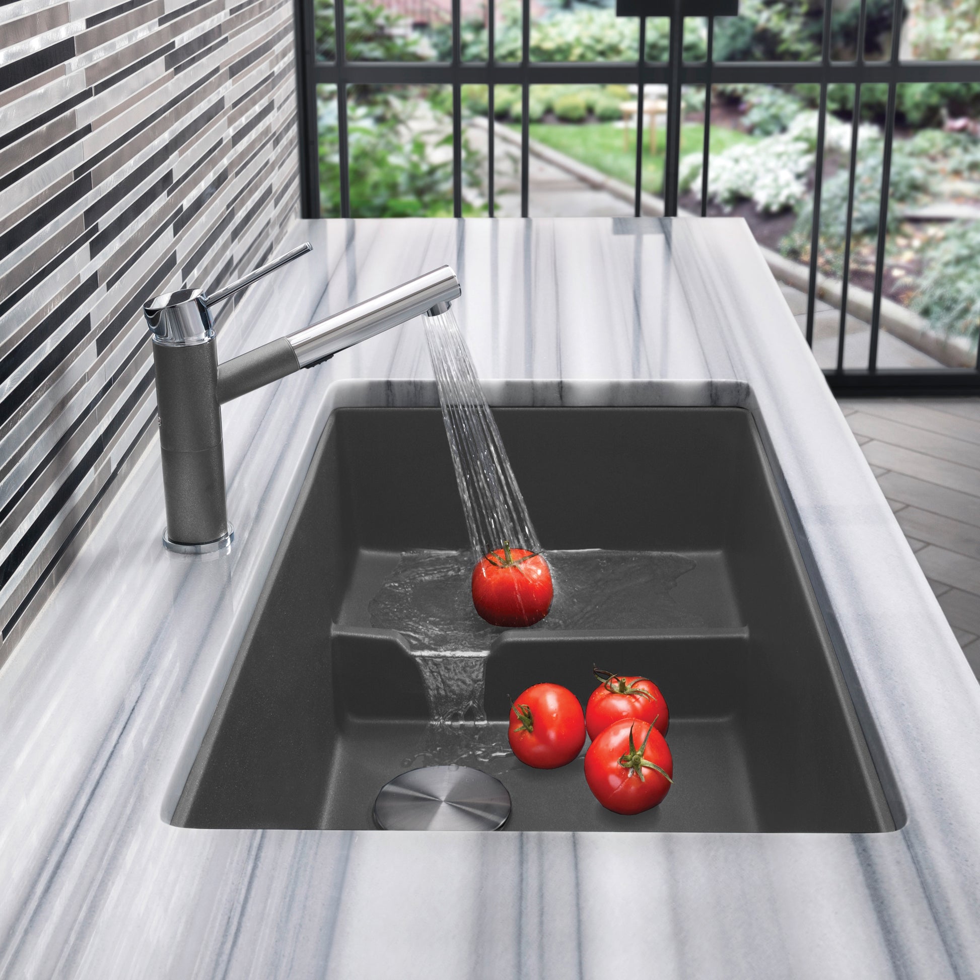 Cinder gray undermount kitchen sink with single basin and matching pull-down faucet, water running over tomatoes.