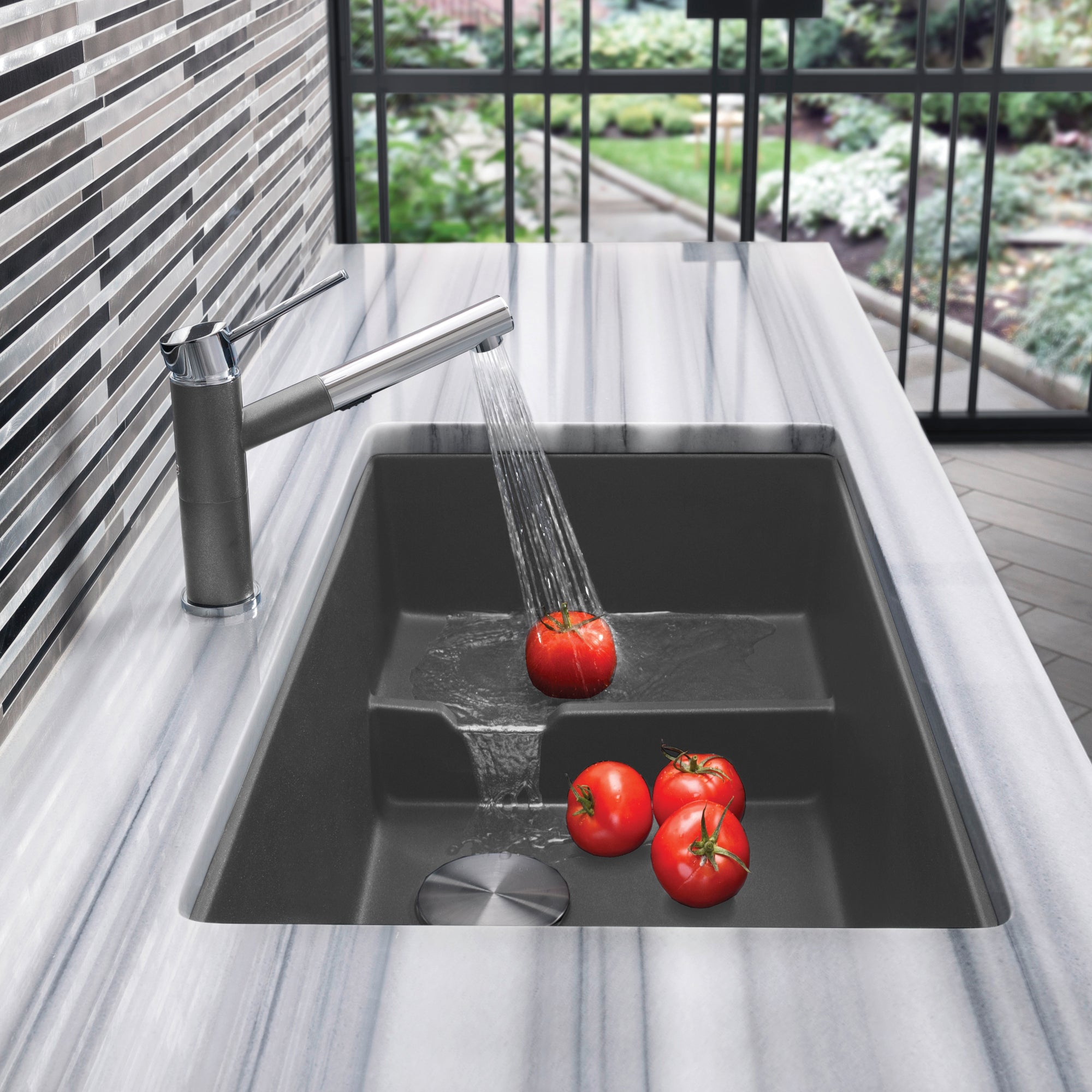 Cinder gray undermount kitchen sink with single basin and matching pull-down faucet, water running over tomatoes.