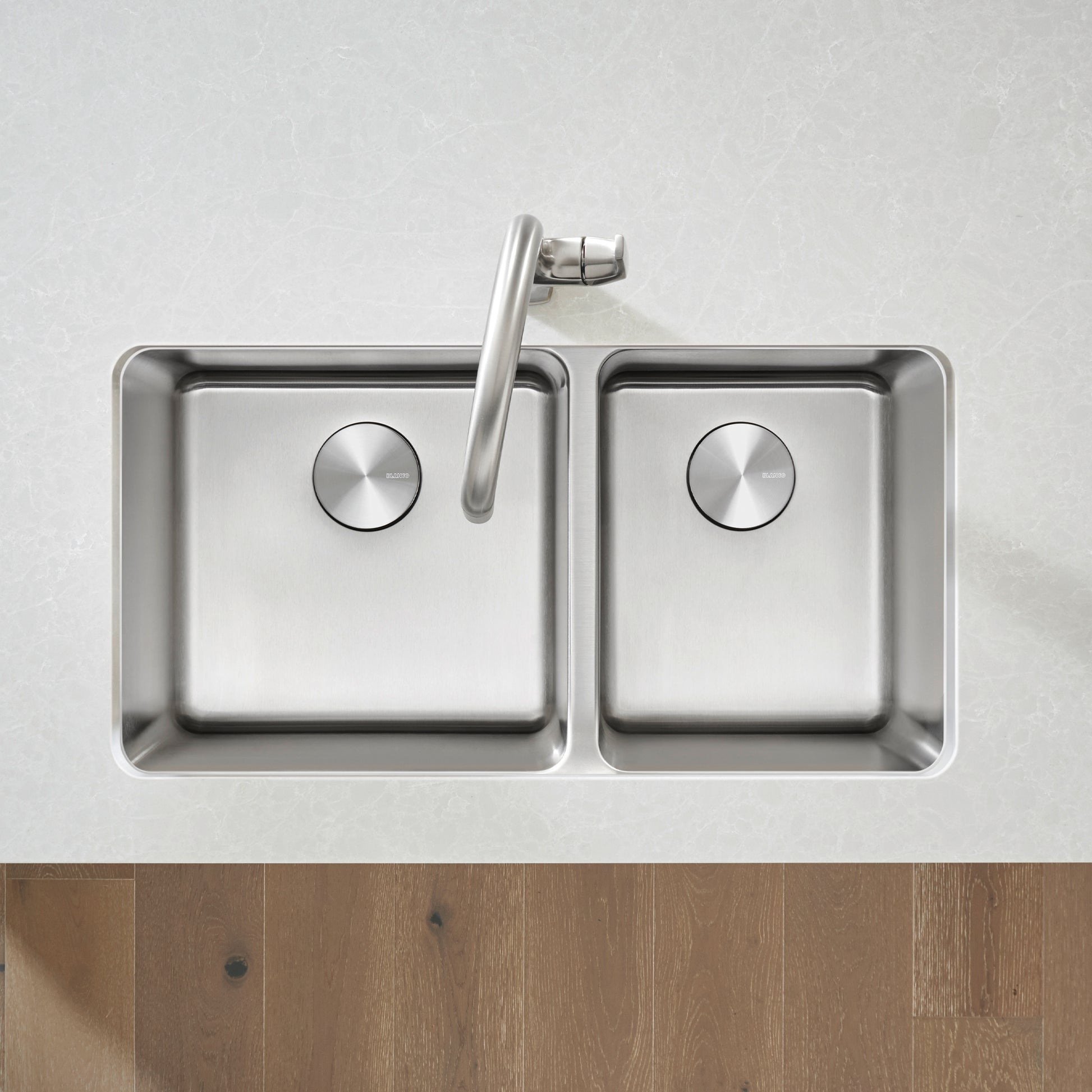 Stainless steel double bowl undermount sink with two drains, faucet spout, and rounded corners viewed from above.