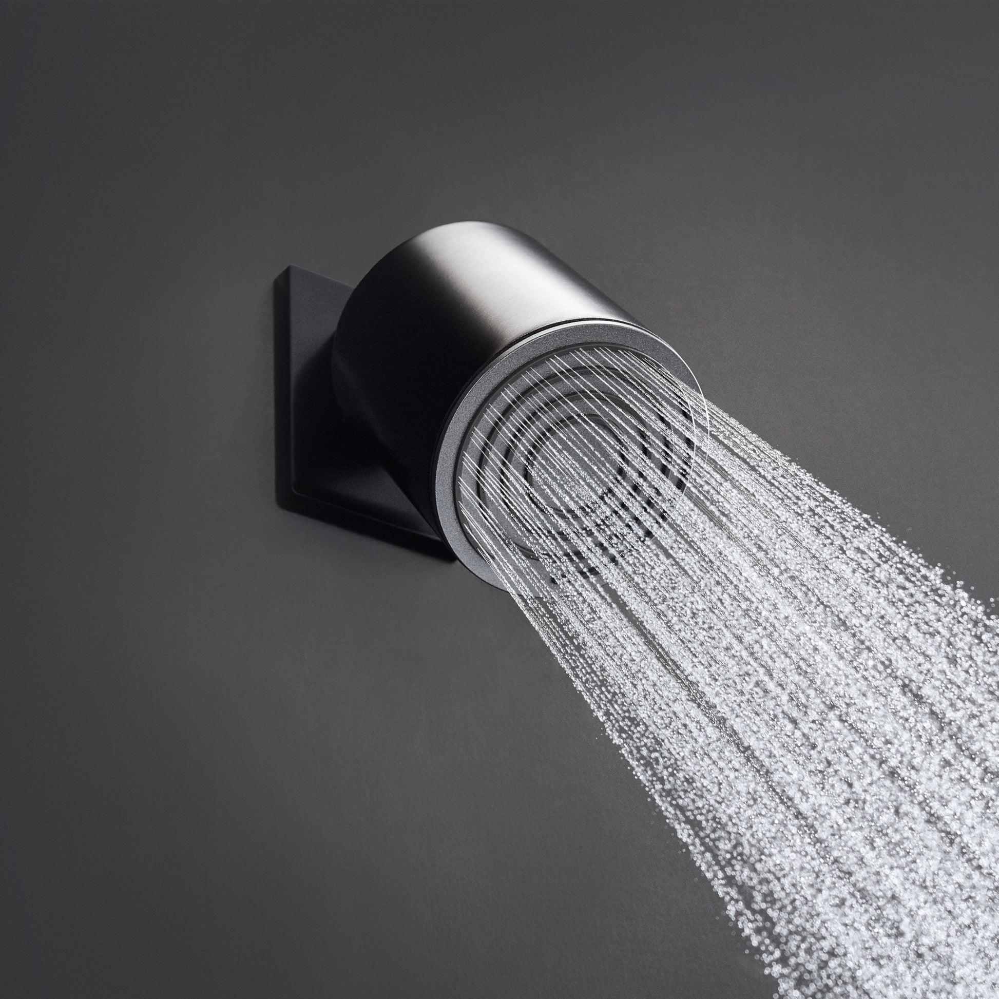Matte black cylindrical shower arm mounted to wall with water spray flowing from outlet.