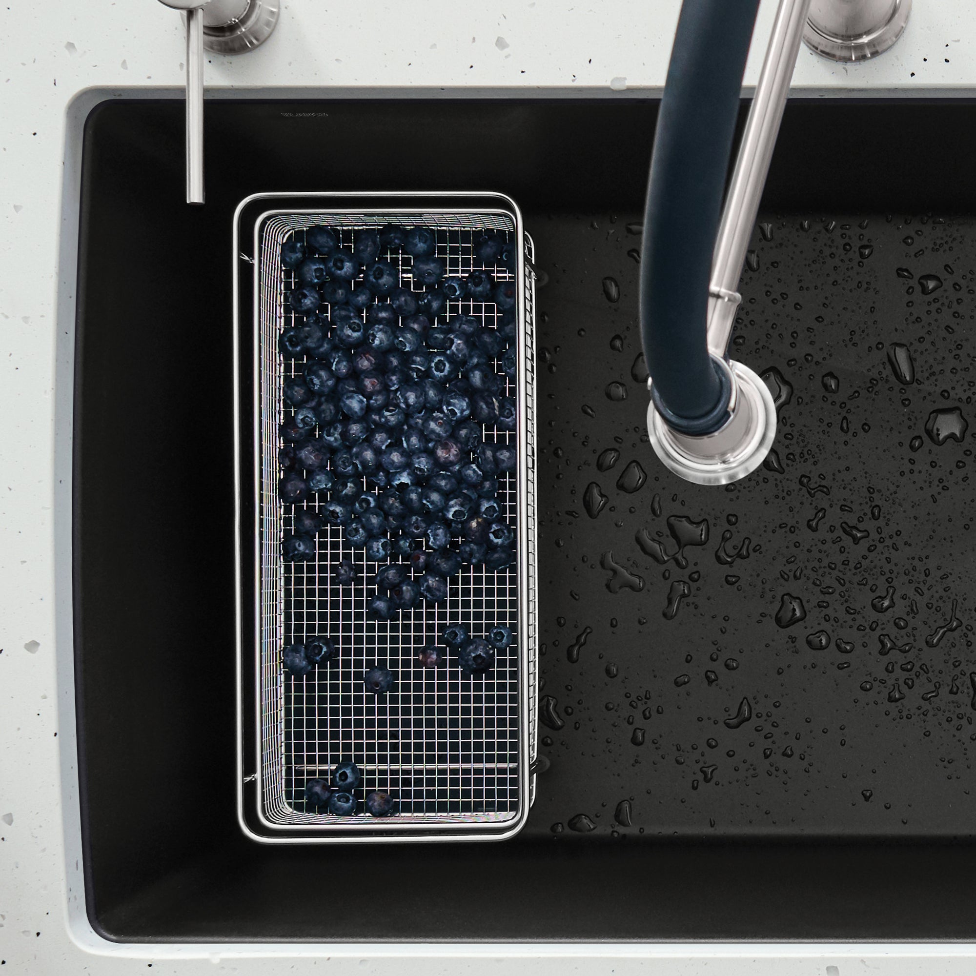 Stainless steel rectangular mesh basket filled with blueberries, positioned in a black sink next to a faucet.