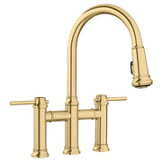 Satin gold bridge faucet with pull-down spray head and two lever handles.