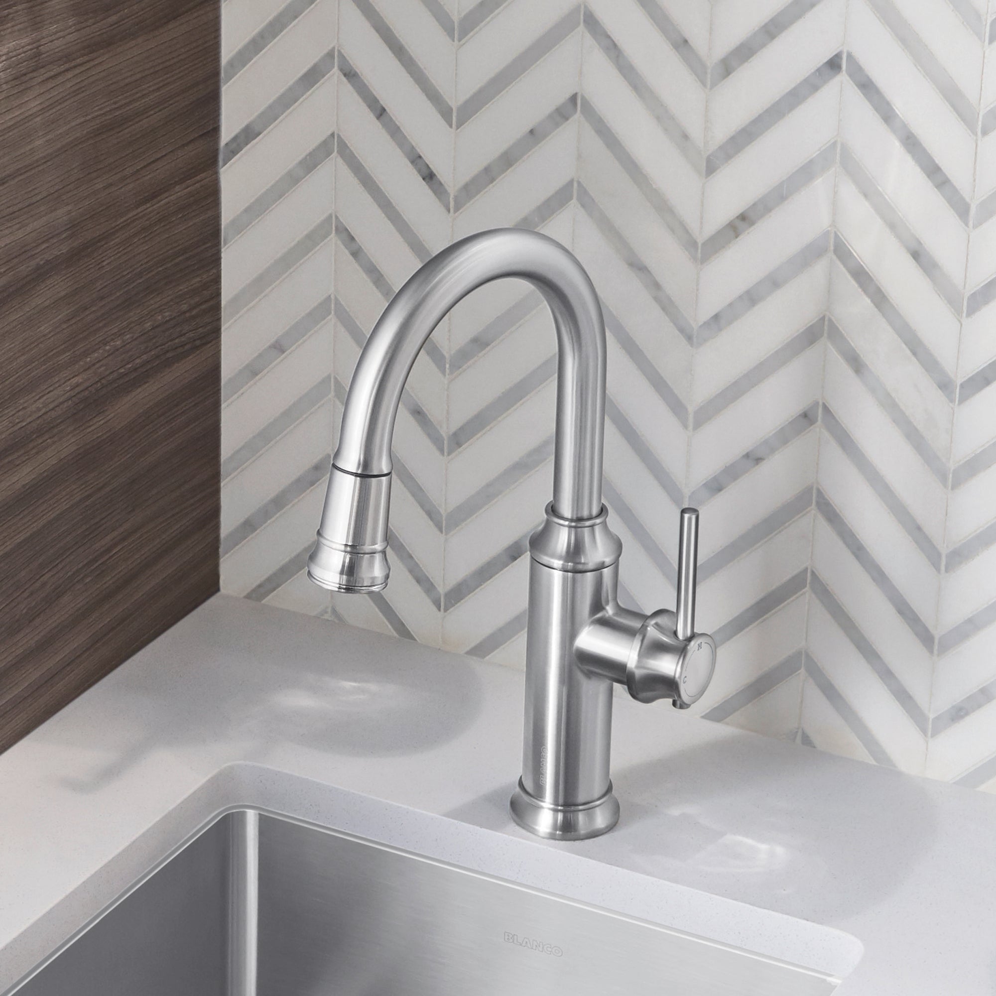 Stainless steel pull-down kitchen faucet with curved spout and single lever handle mounted above white sink.