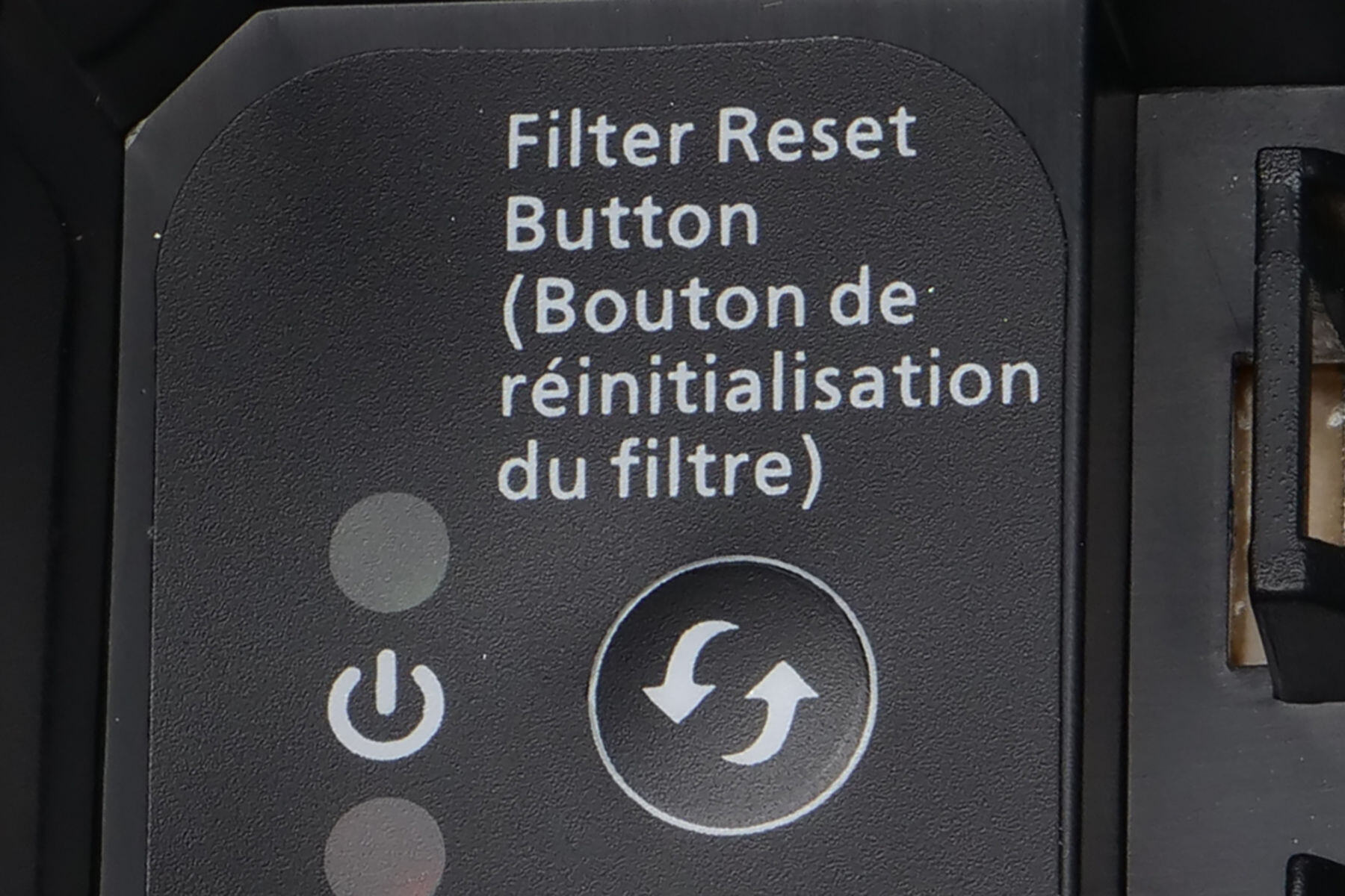 Close-up of black control panel with power button and circular filter reset button with bilingual text labels.
