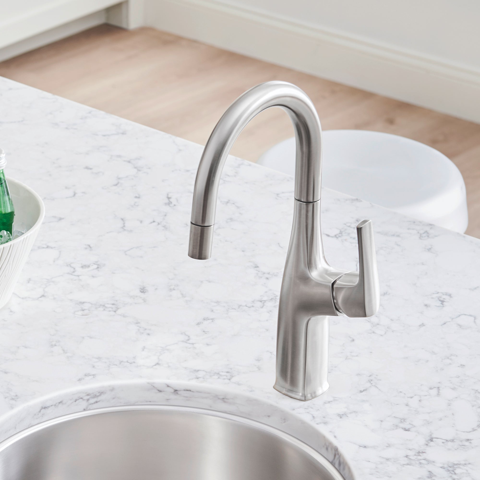 Stainless steel bar faucet with curved spout and single lever handle mounted on marble countertop above sink.