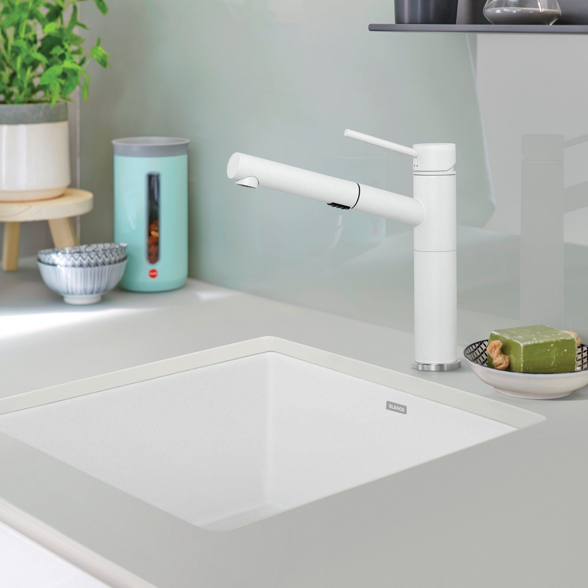 White undermount kitchen sink bowl installed in countertop with white faucet.
