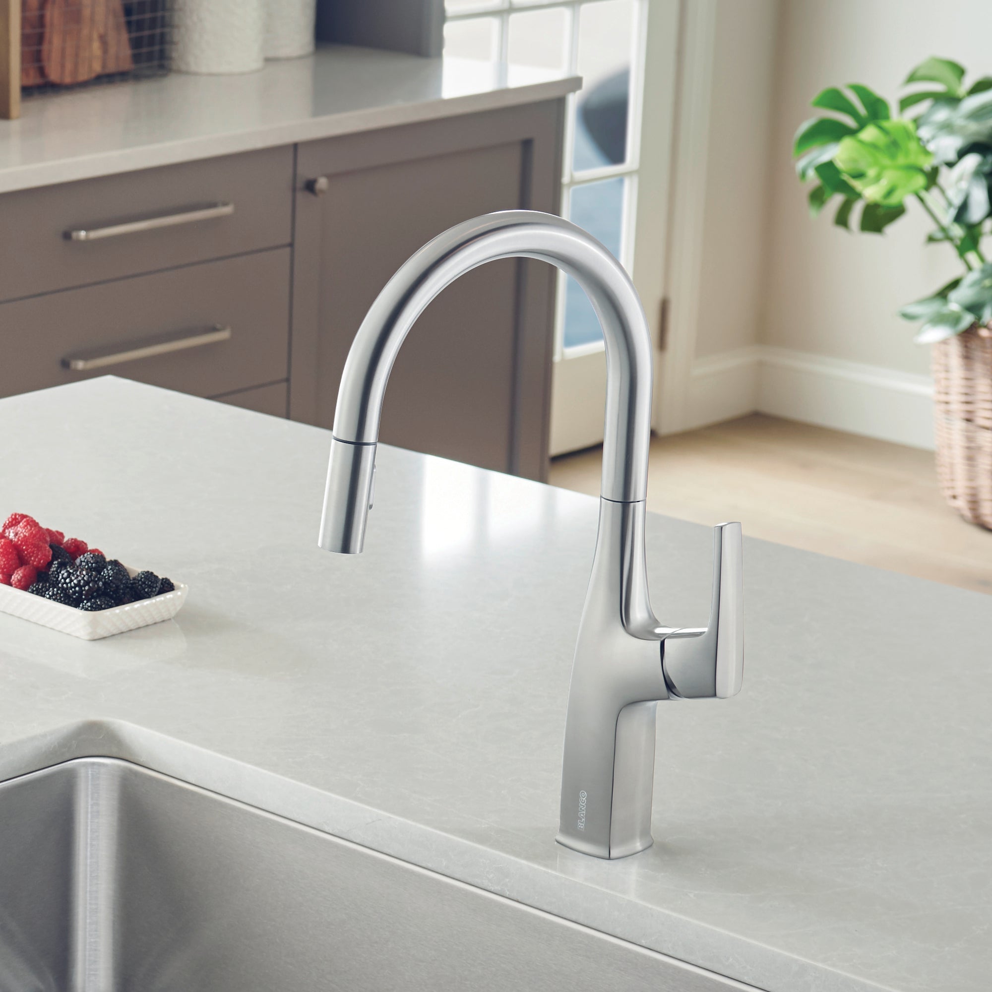 Stainless steel pull-down kitchen faucet with curved spout and lever handle mounted on white countertop above sink.