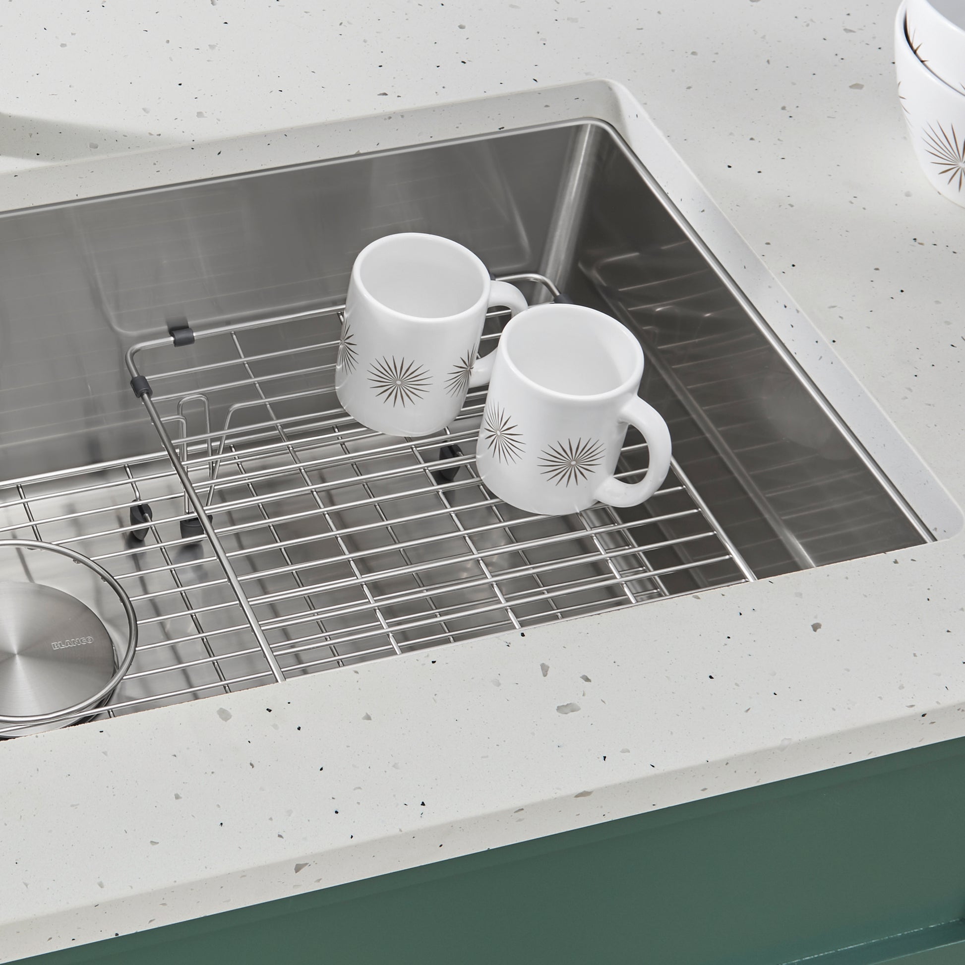 Stainless steel multi-level sink grid with two white mugs and cookware inside a single bowl sink.