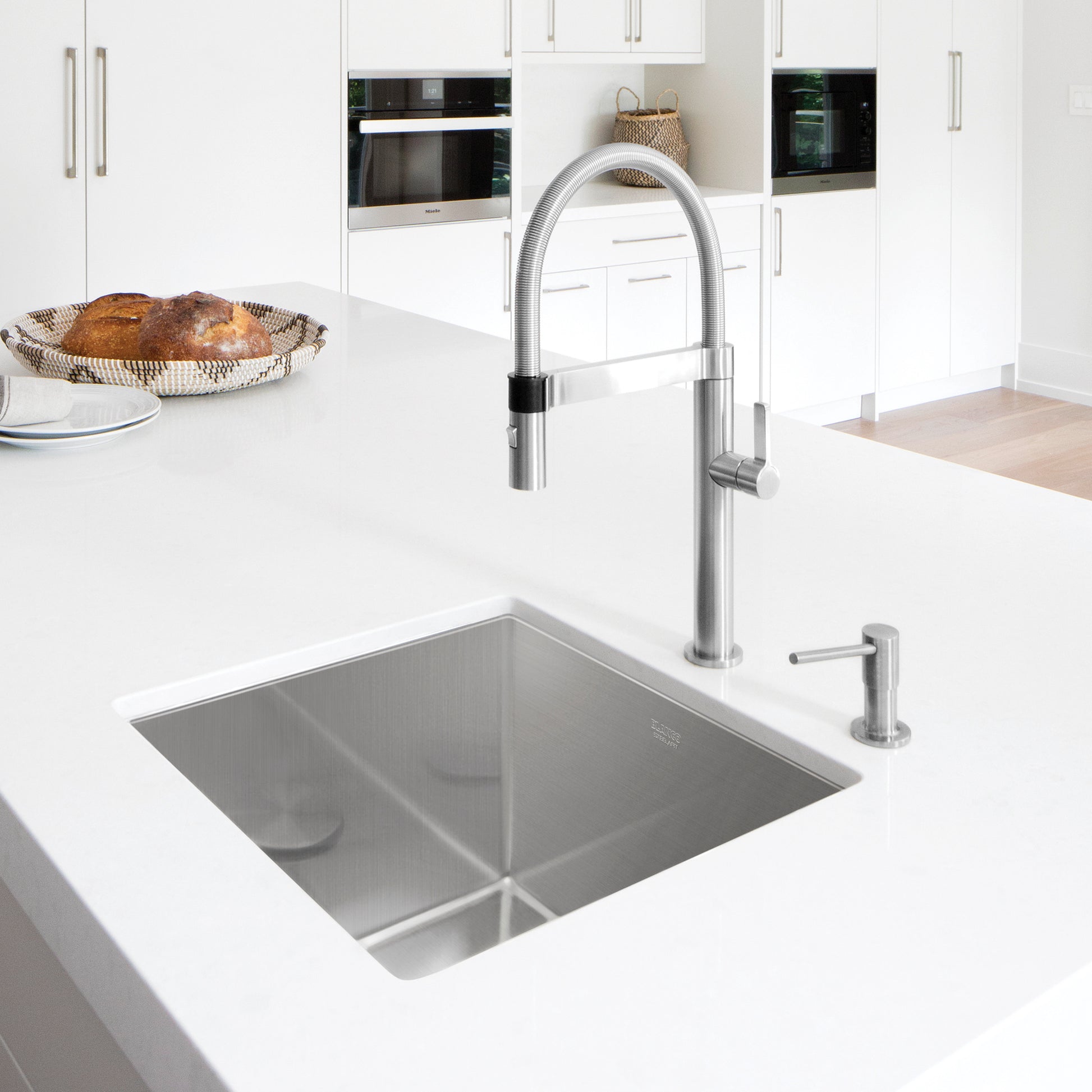 Stainless steel single bowl undermount sink installed in white countertop with pull-down faucet and soap dispenser.