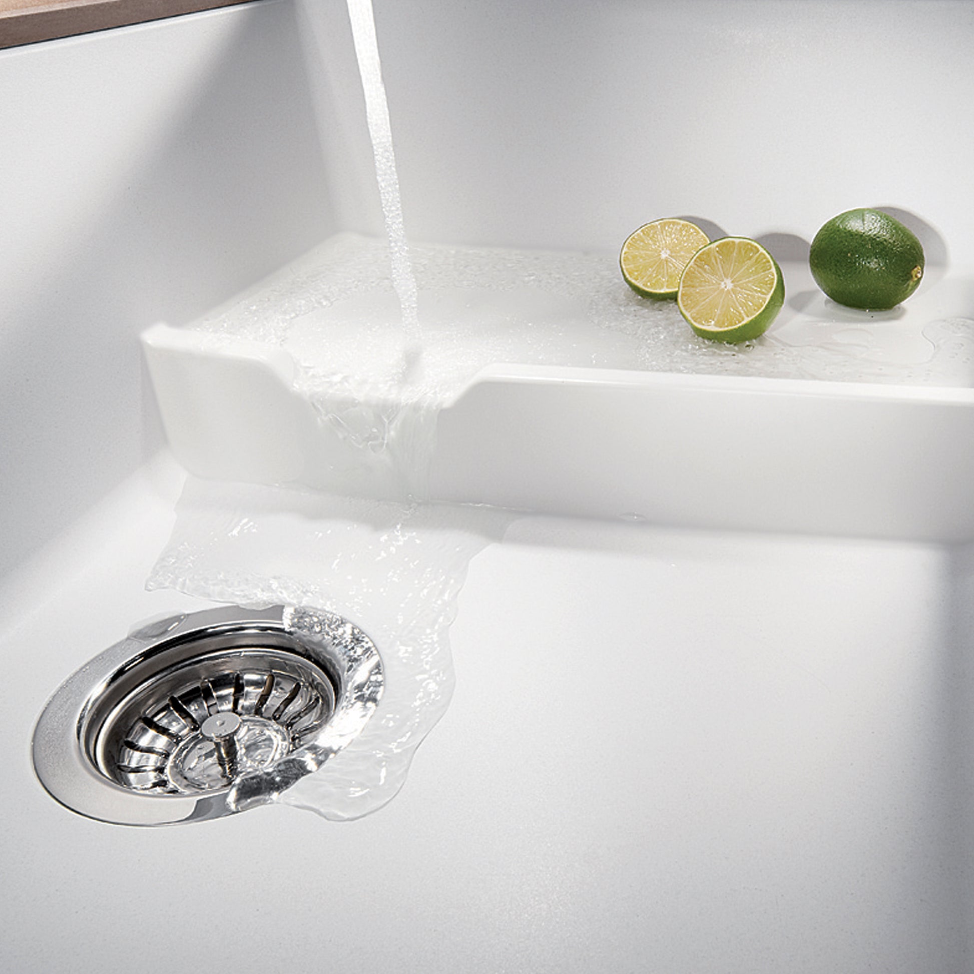 White undermount kitchen sink with single basin, chrome drain, and water flowing into basin with lime slices nearby.