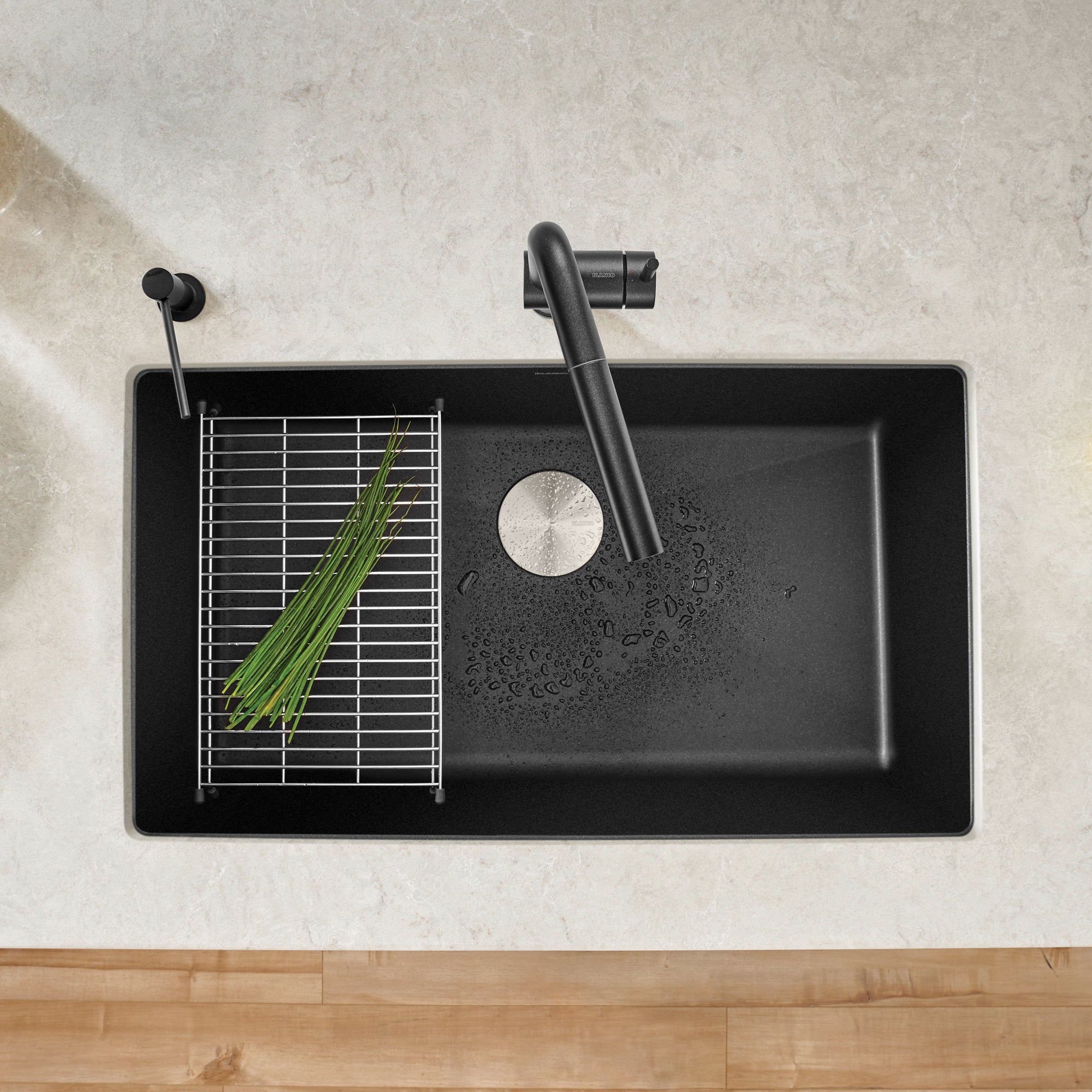 Anthracite undermount kitchen sink with single bowl, drain strainer, and black faucet, viewed from above.