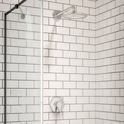 Chrome round shower head mounted on wall with perforated spray pattern and curved arm in tiled shower enclosure.