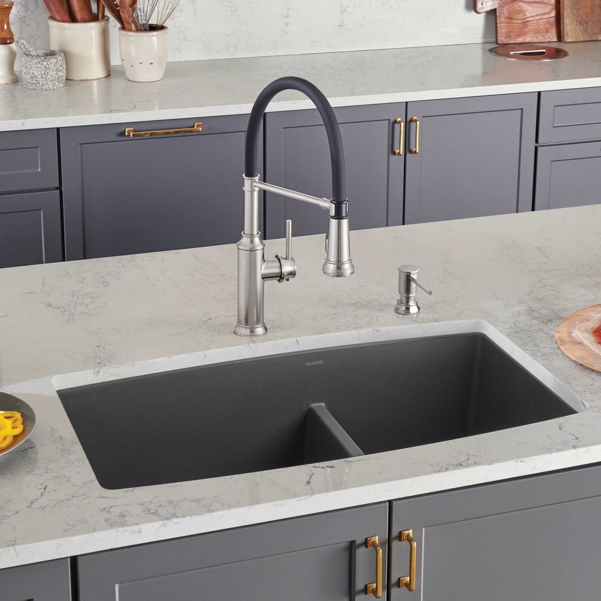 Cinder undermount kitchen sink with two unequal bowls and stainless steel faucet installed in marble countertop.