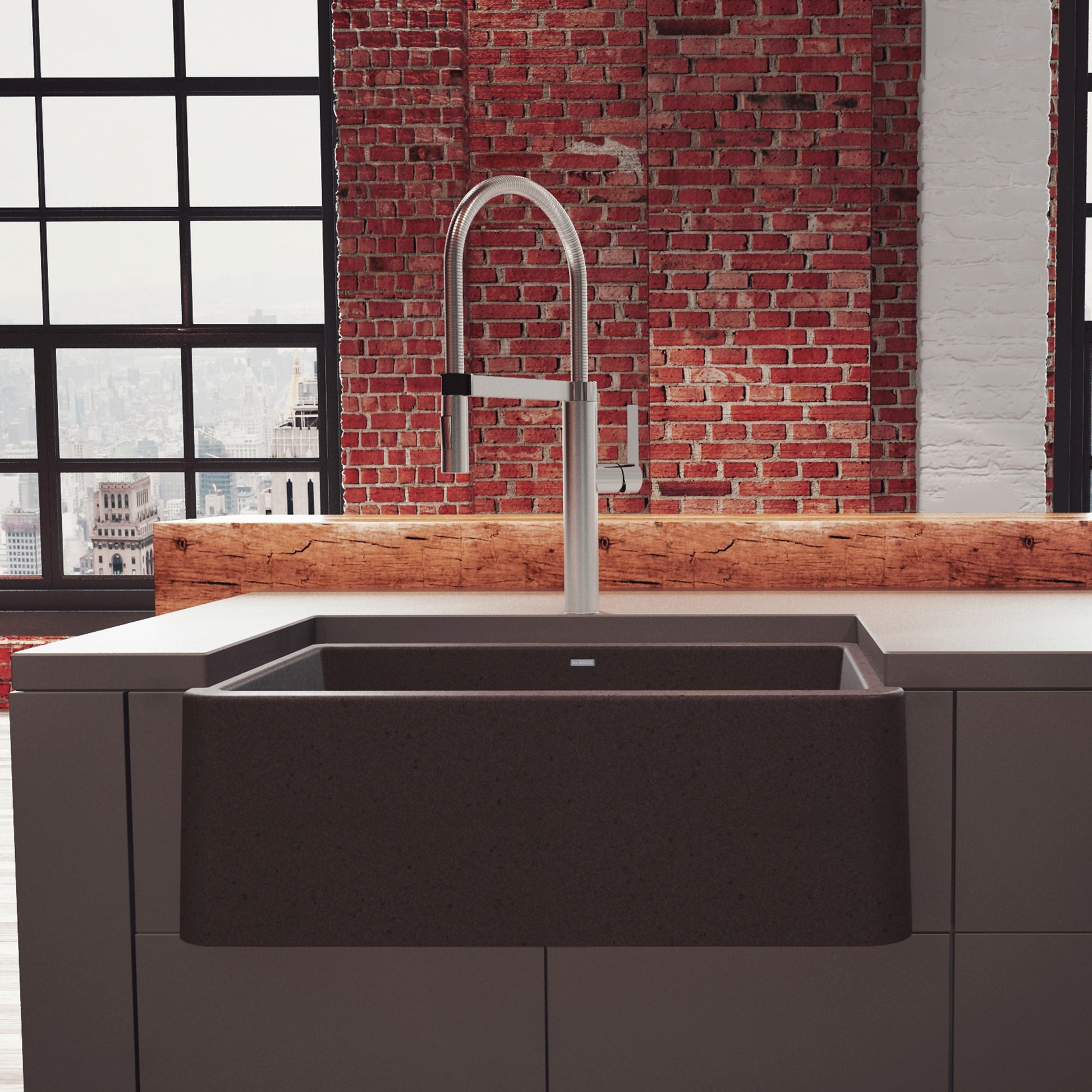 Cafe brown apron front kitchen sink with arched chrome faucet installed in countertop, industrial window and brick backdrop.