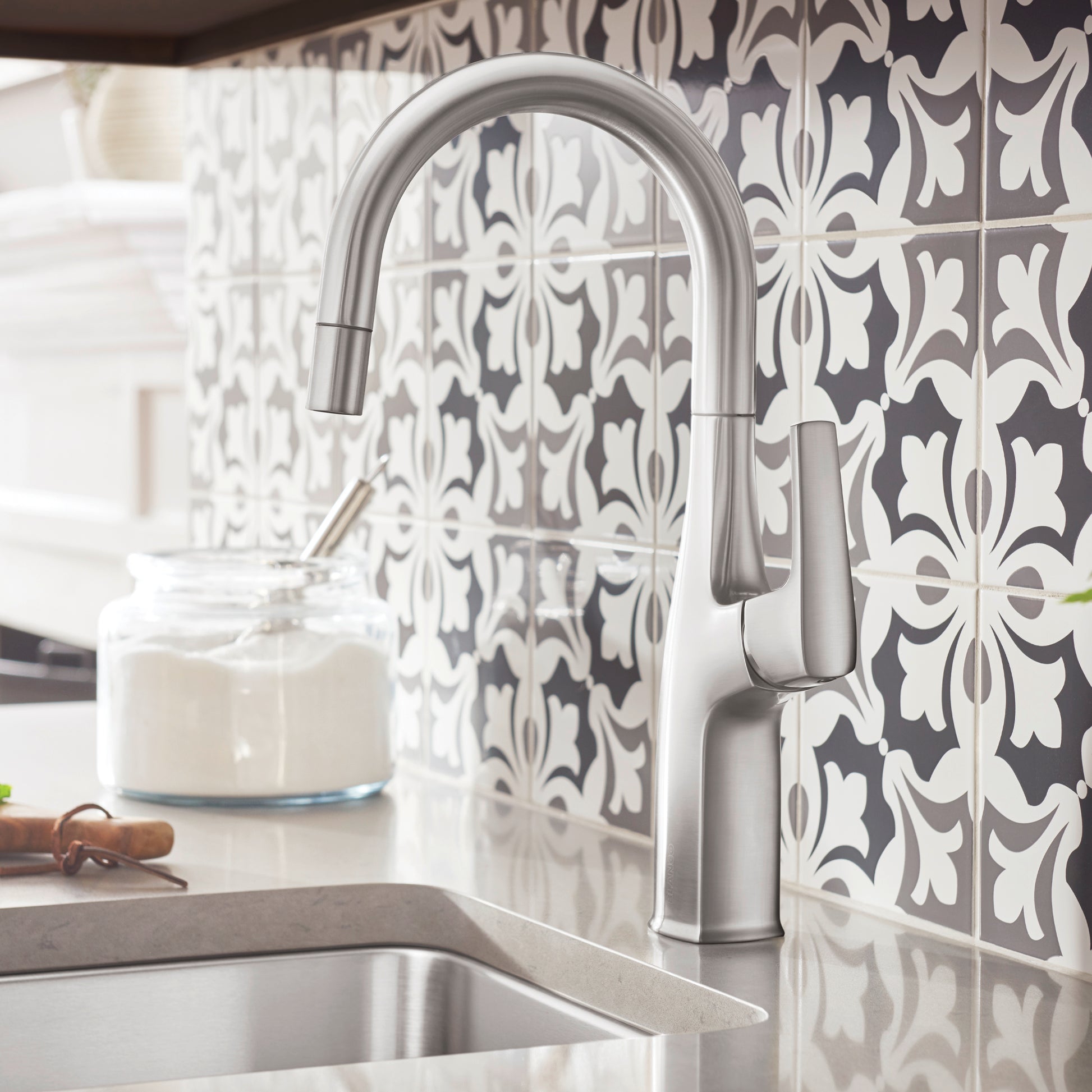 Stainless steel bar faucet with curved spout and pull-down sprayer over sink.