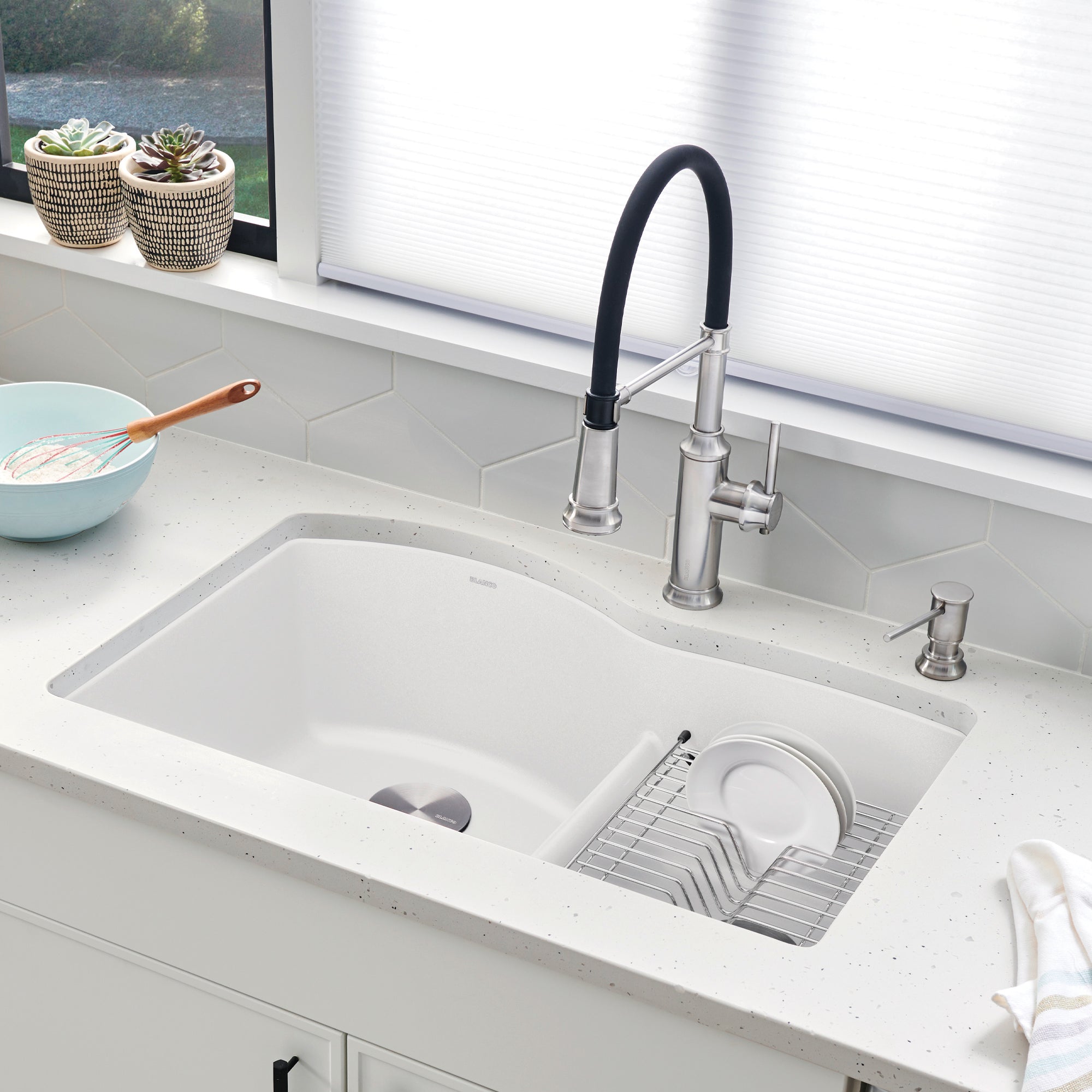 White undermount kitchen sink with divided compartments, stainless steel faucet with black handle, and dish rack insert.
