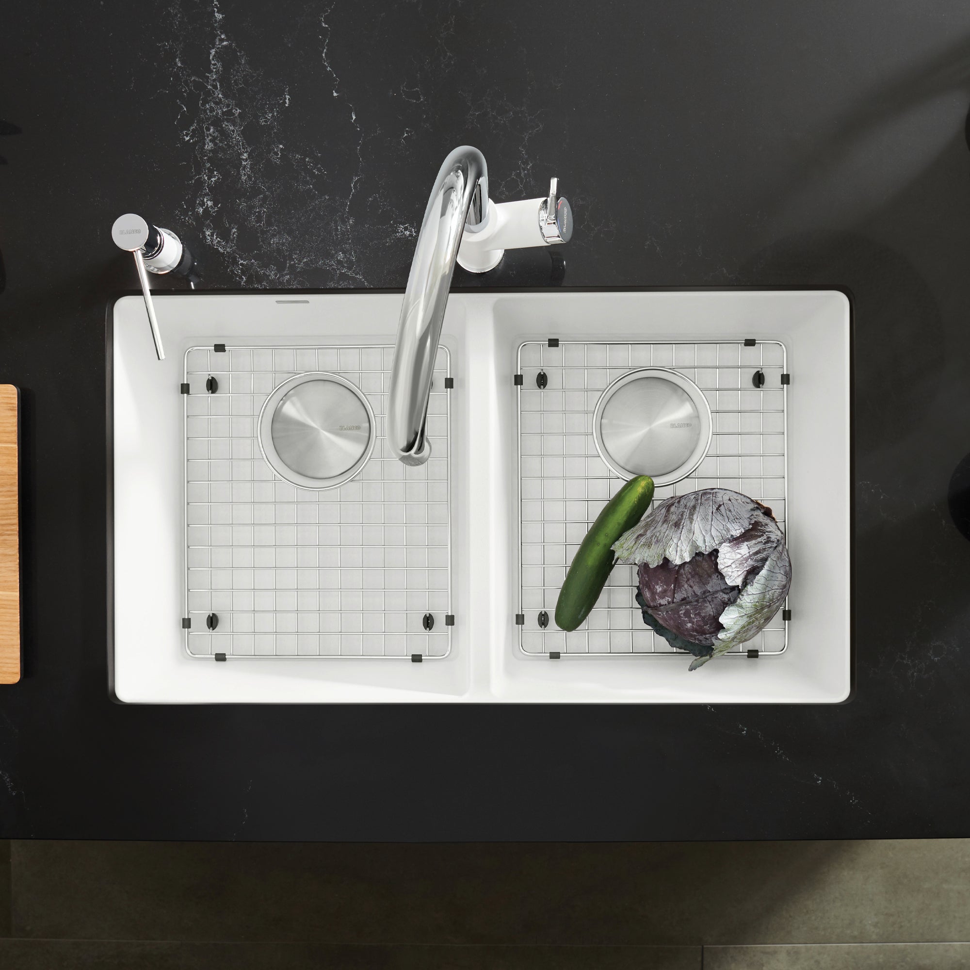 Stainless steel sink grid with small square pattern positioned in white double bowl sink with vegetables and faucet.