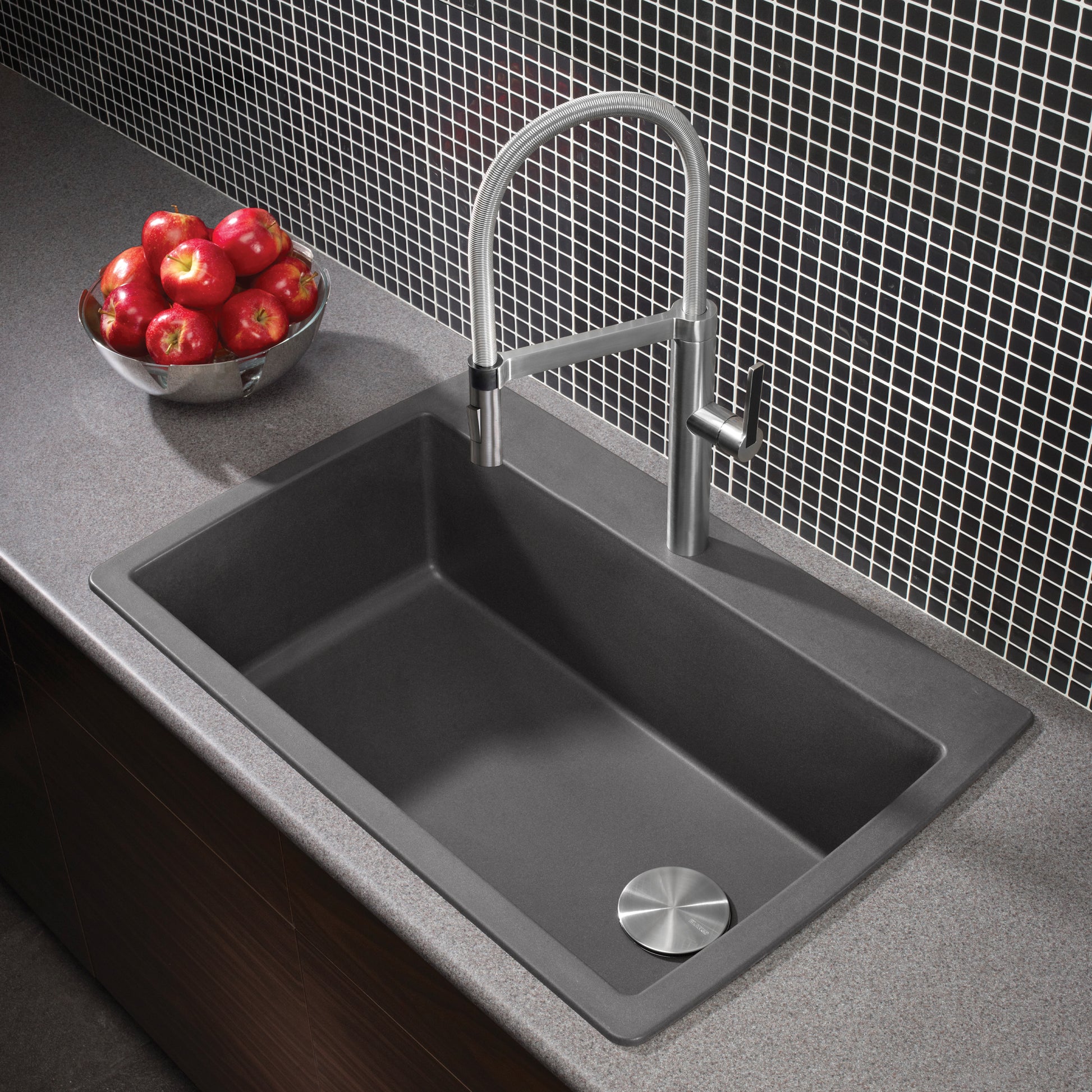 Dark gray composite drop-in kitchen sink with single bowl, chrome faucet, and drain strainer on countertop.