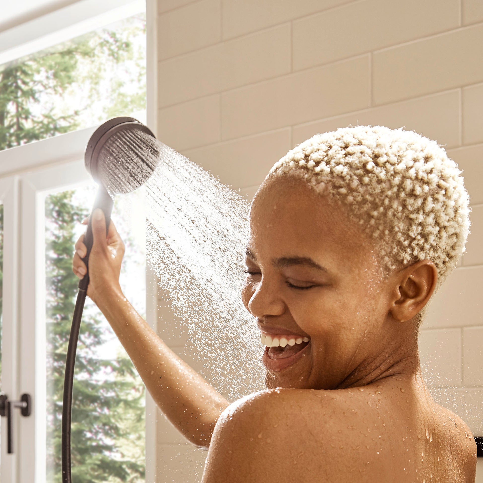 Matte black handheld showerhead with 3-jet spray pattern dispensing water in a bathroom setting.