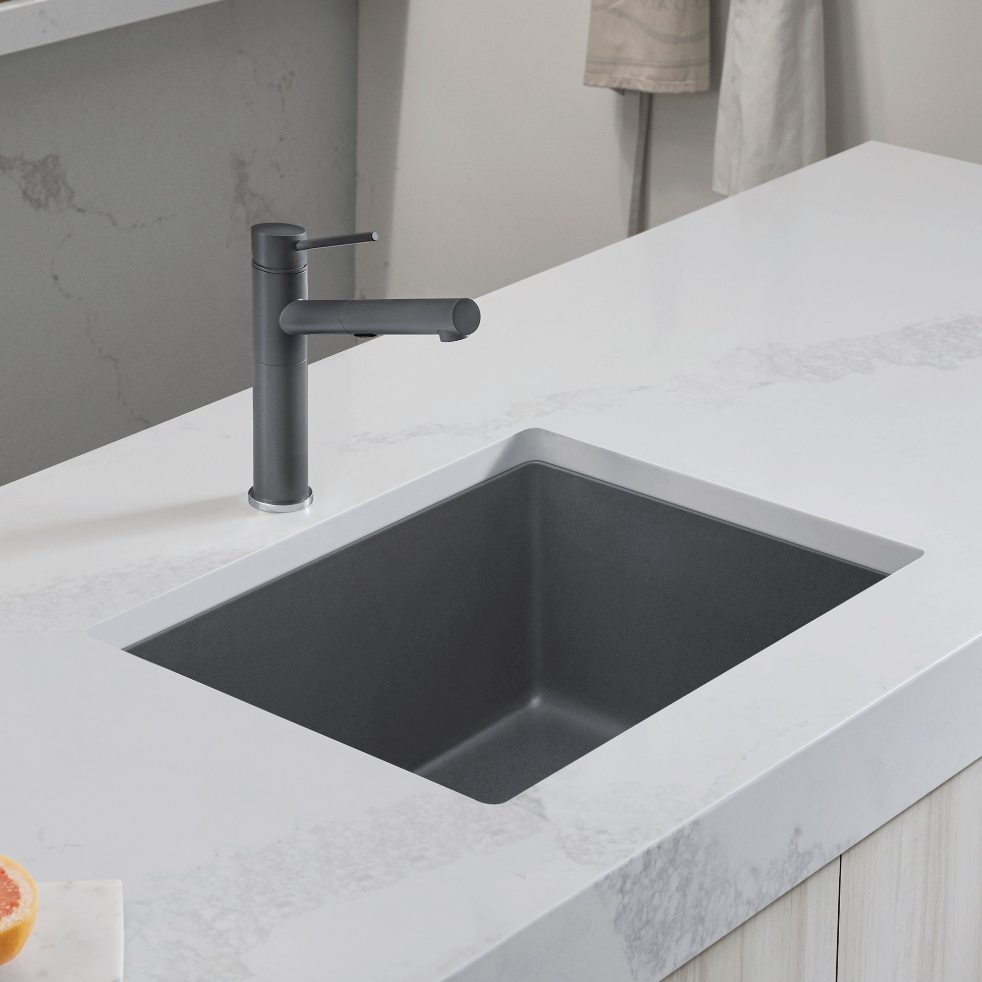 Dark gray rectangular kitchen sink with single black faucet installed in white marble countertop.