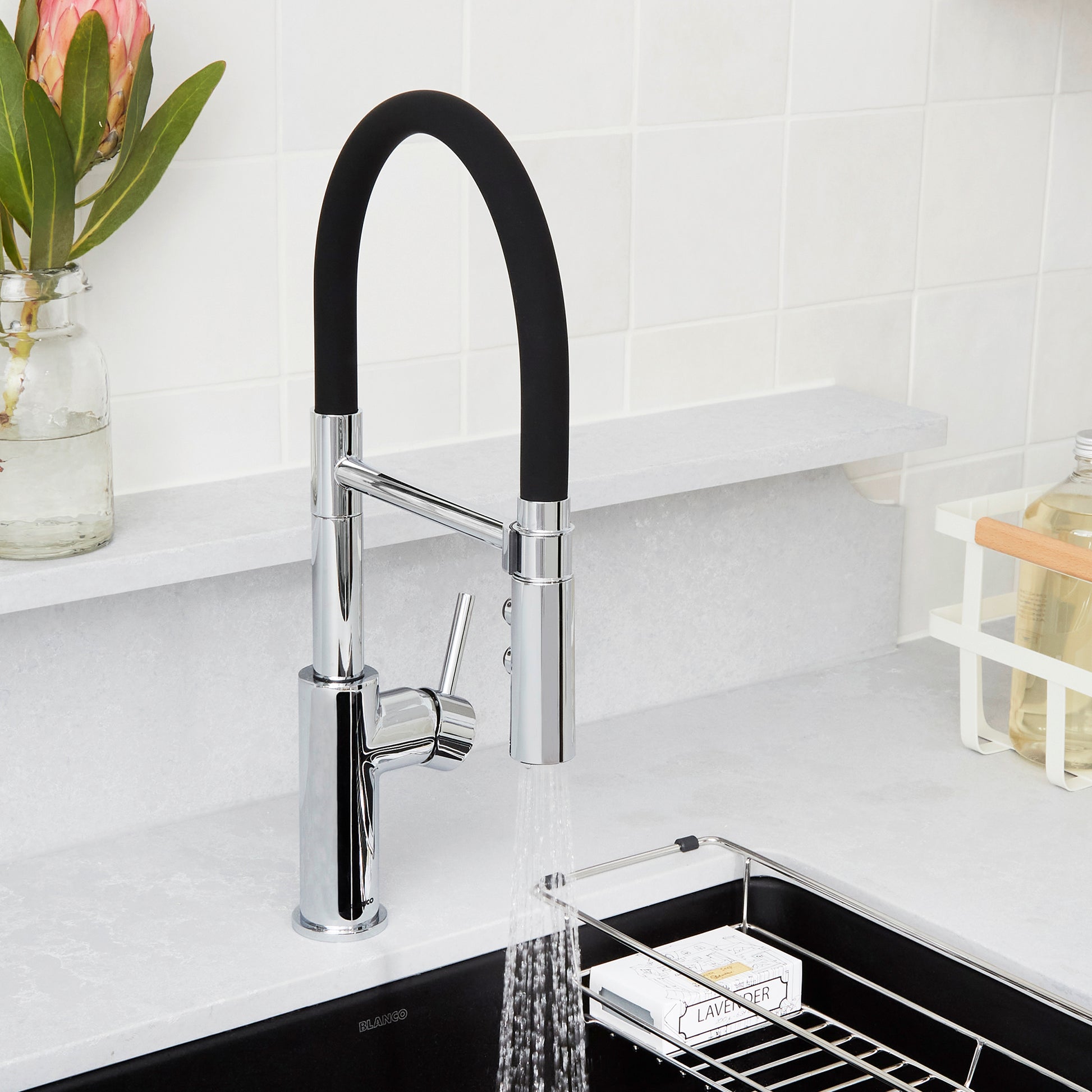 Chrome kitchen faucet with black flexible hose and single lever handle above black sink basin.