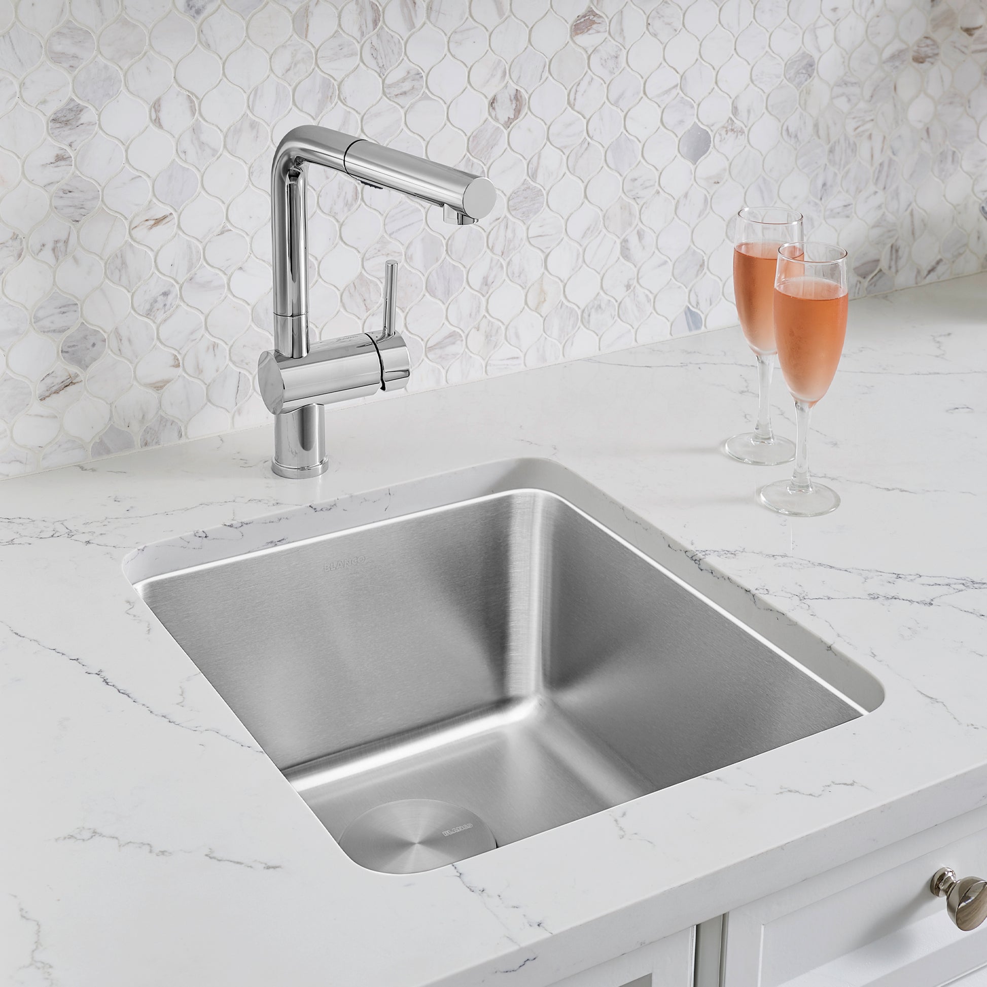 Stainless steel undermount bar sink with two compartments and chrome pull-down faucet on marble countertop.