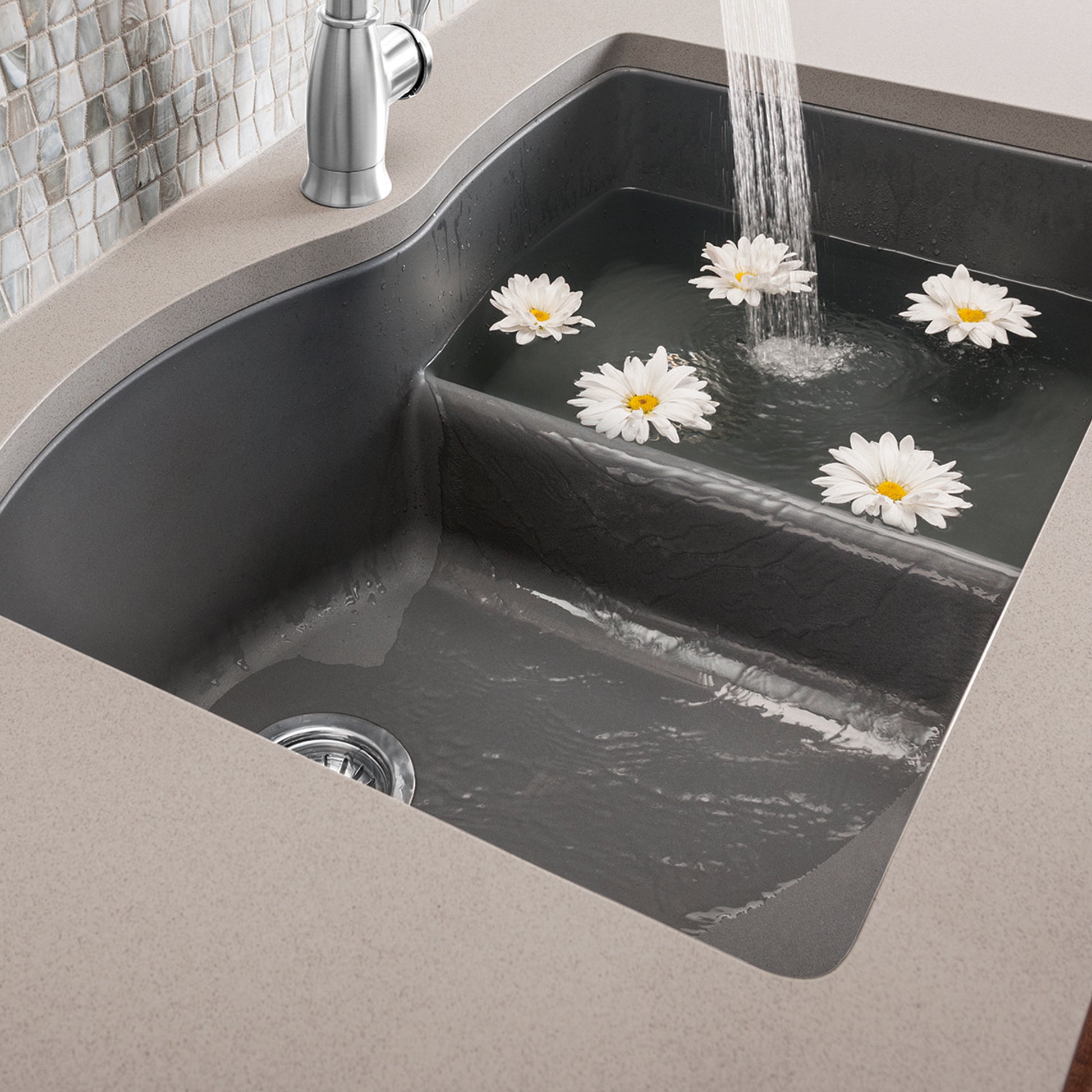 Cinder-colored undermount kitchen sink with low divide, chrome faucet, and water running into one basin.