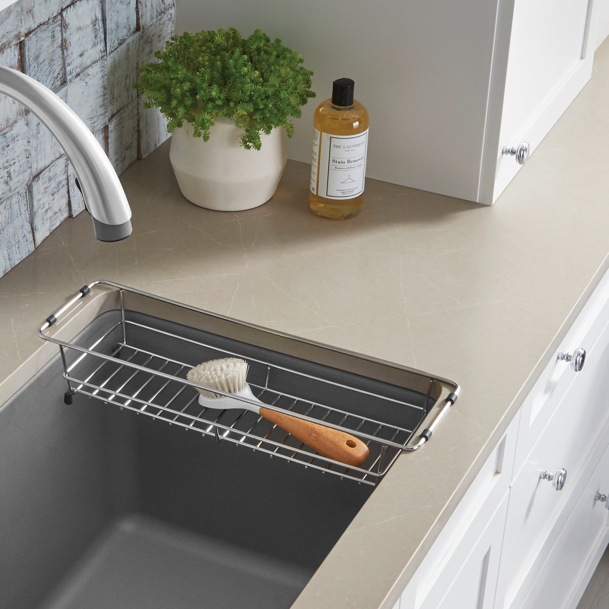Stainless steel rectangular basket with handles positioned inside a laundry sink, containing a brush.