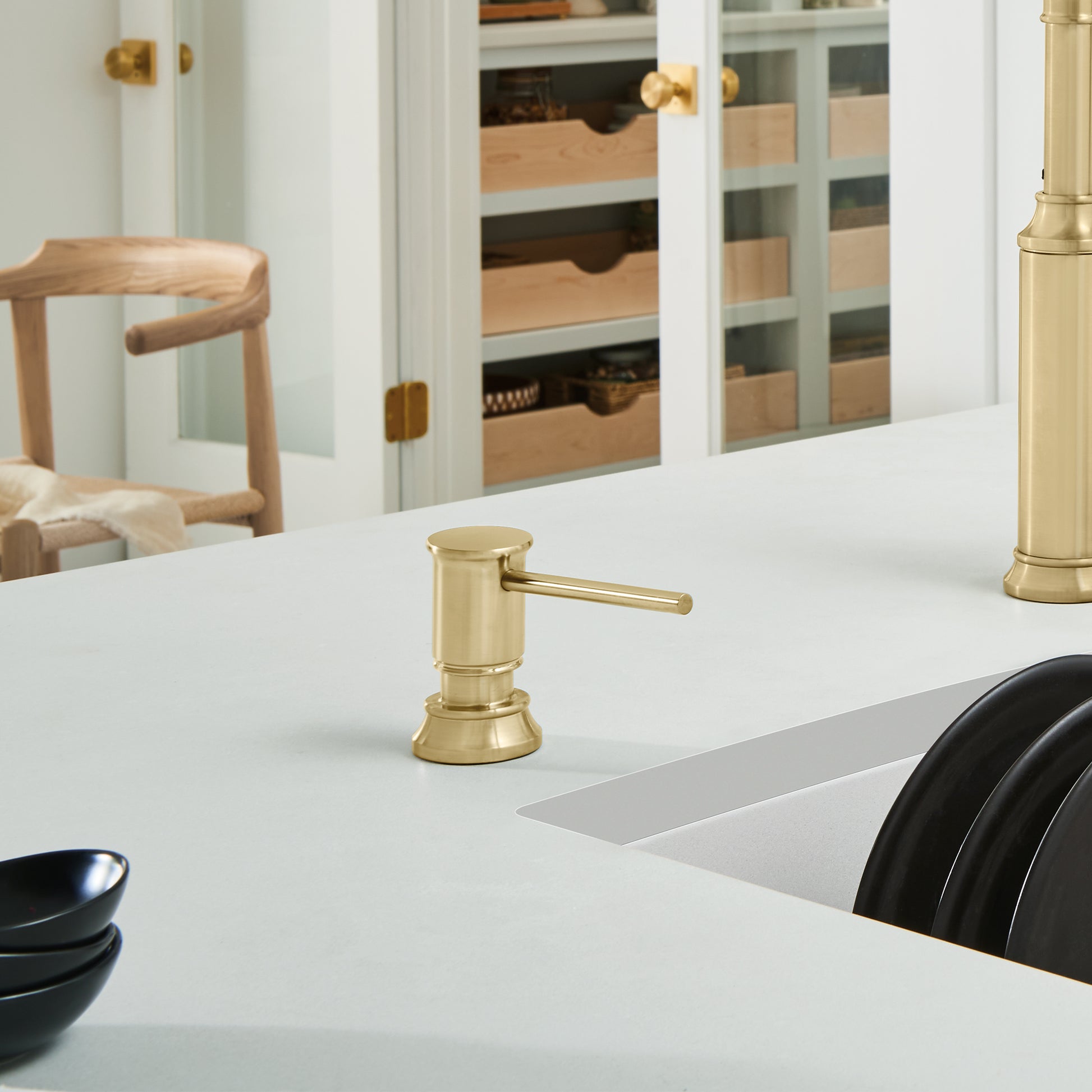 Satin gold soap dispenser with cylindrical pump and lever spout on white countertop.
