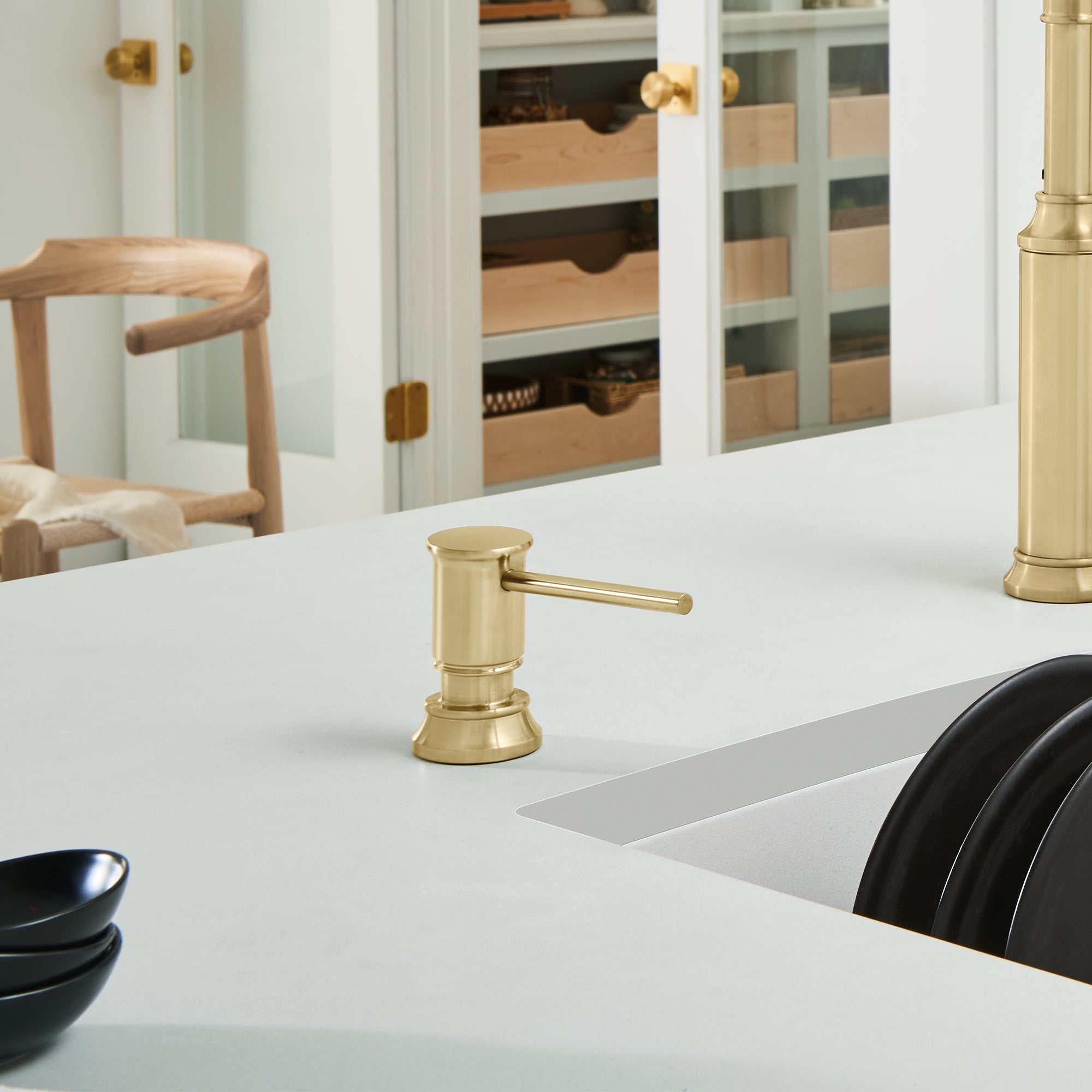 Satin gold soap dispenser with cylindrical pump and lever spout on white countertop.