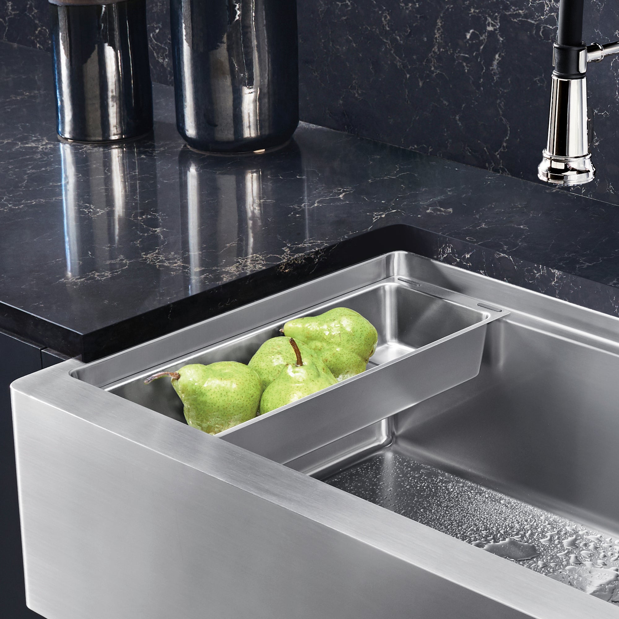 Stainless steel colander insert fitted in kitchen sink basin with green pears inside.