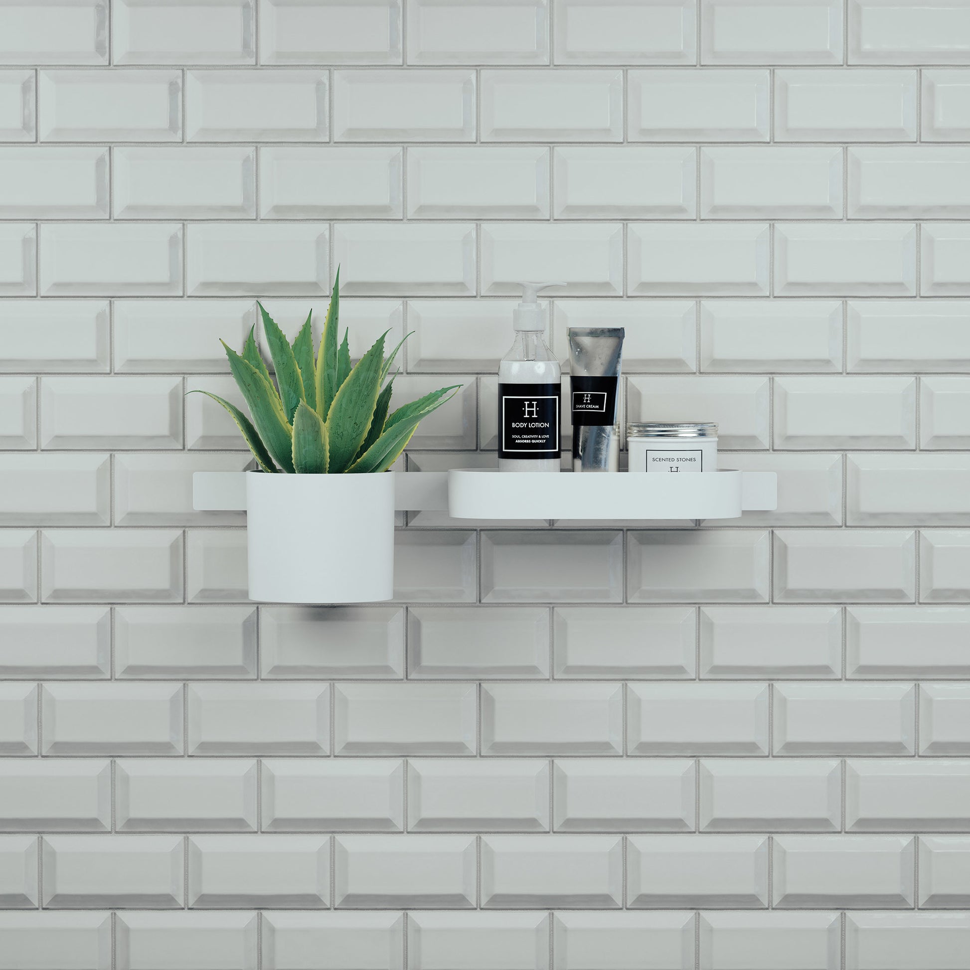 Matte white wall-mounted shelf with tumbler, cosmetic bottles, and potted succulent against white subway tile.
